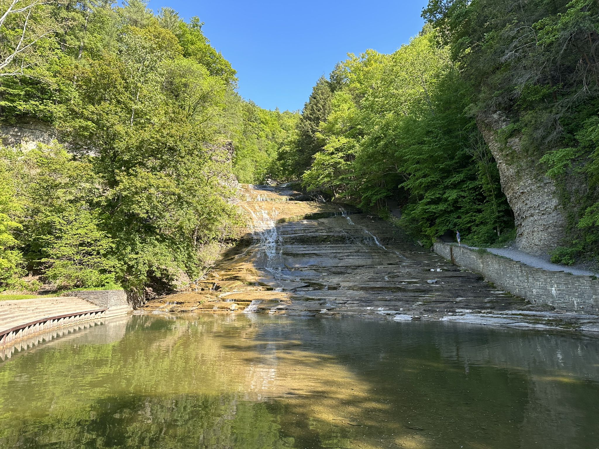 Gentle waterfall flows over wide layered rocks into a calm green pool. - Lake Treman – Buttermilk Falls loop from Buttermilk Falls State Park