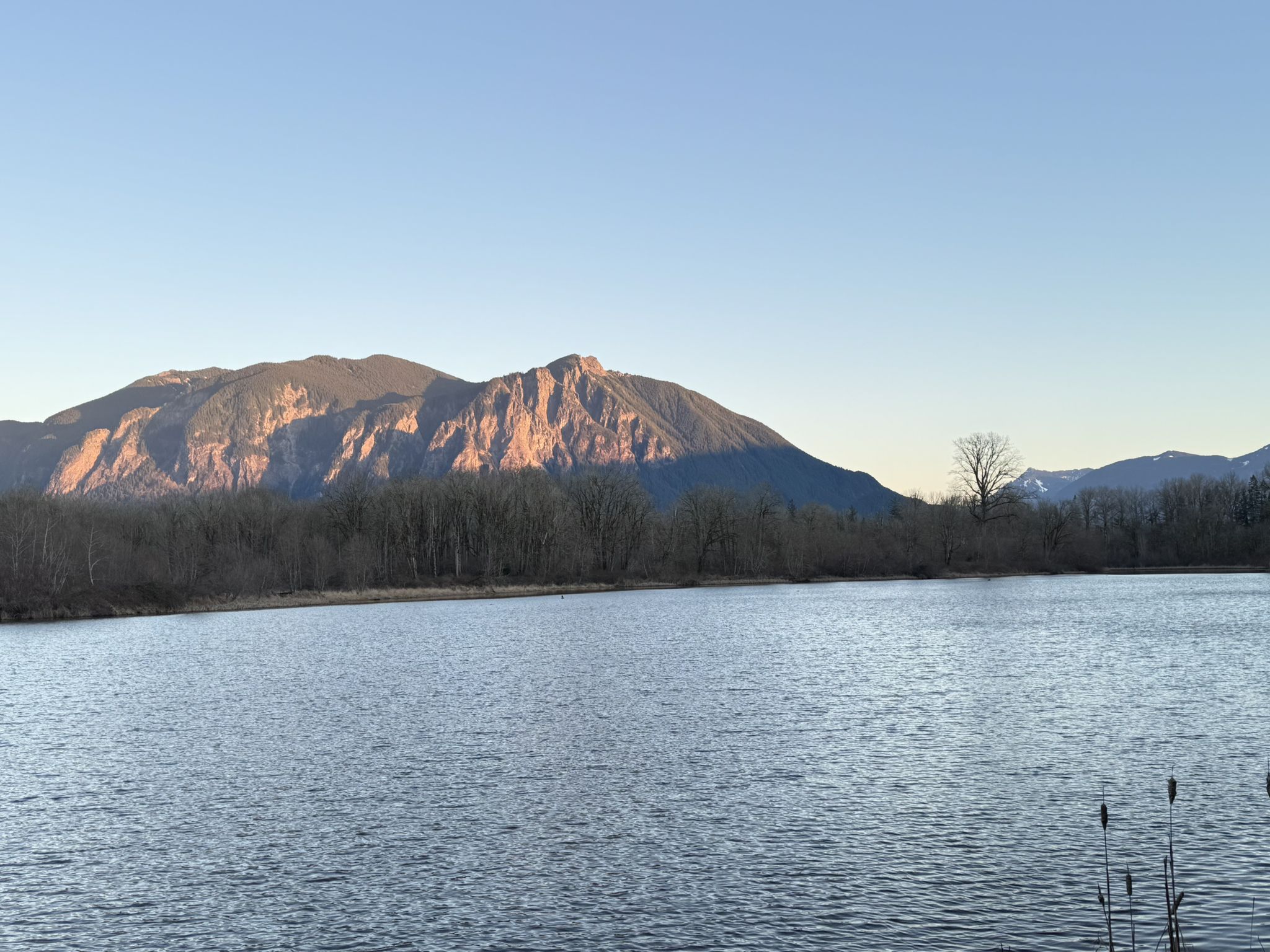 Calm lake reflecting a sunlit mountain range with bare trees. - Snoqualmie Valley Trail Loop