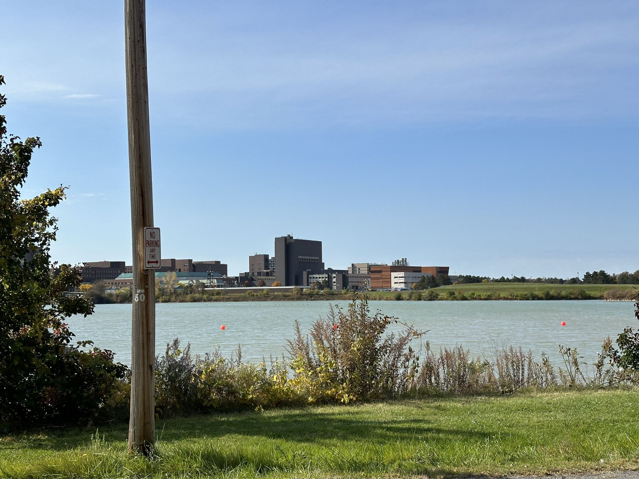 A wide lake with distant buildings under a clear blue sky. - Running loop from University at Buffalo