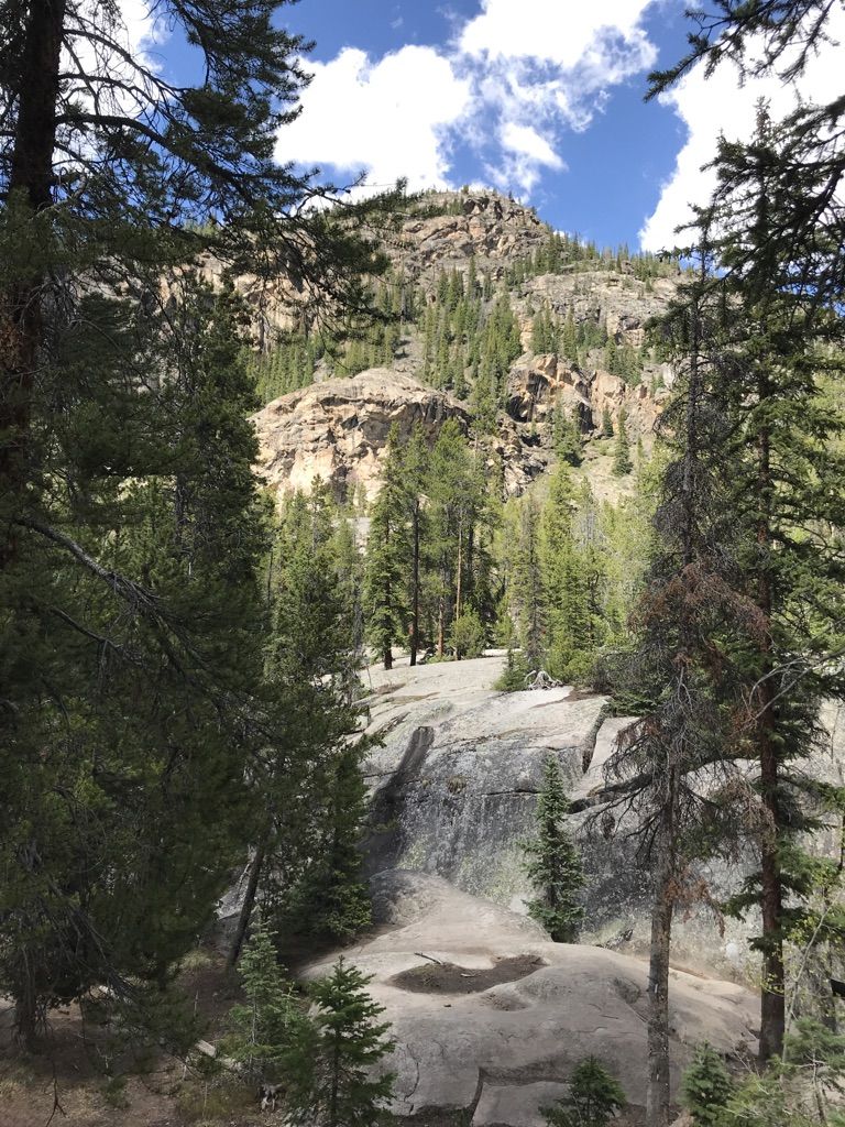 Rocky mountain slopes and pine forest under a bright, partly cloudy sky. - The Grottos Trail