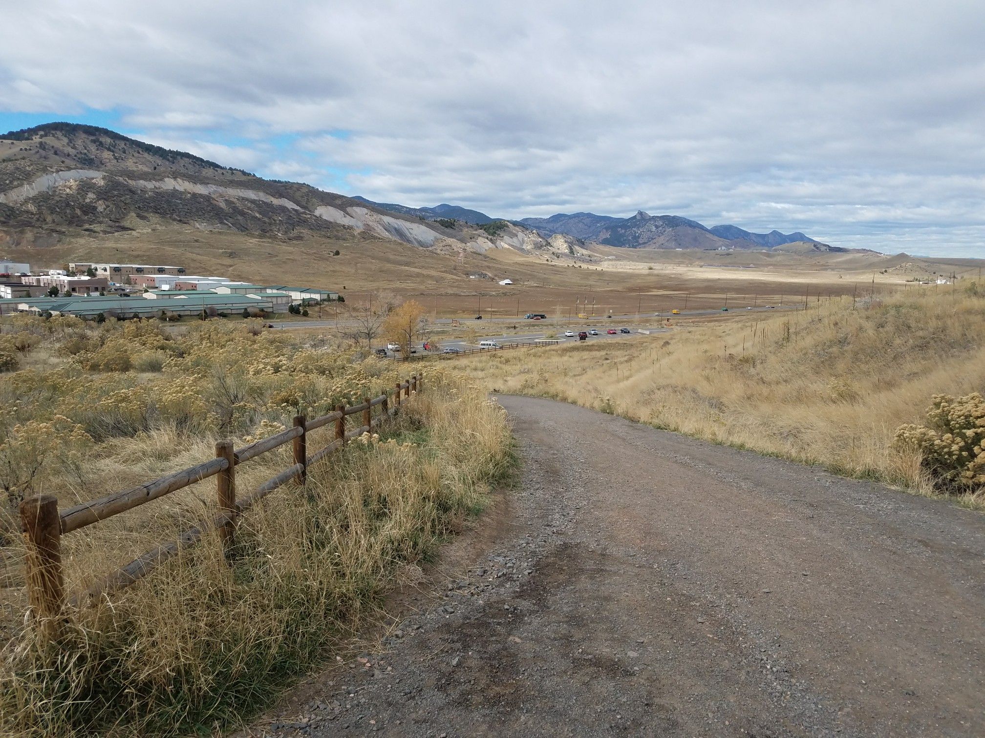 Dirt path with wooden fence leading to a valley and mountains under cloudy sky. - Golden Cliffs Trail