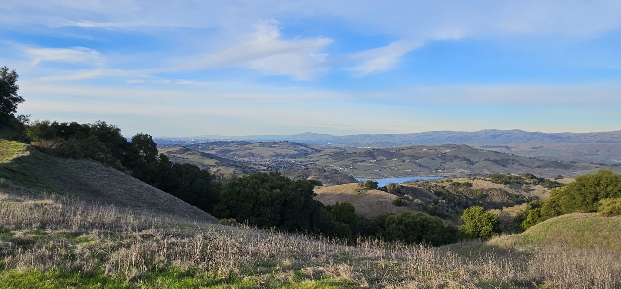 Rolling hills, distant lake, and bright sky under scattered clouds. - Figueroa and Cottle Loop Trail