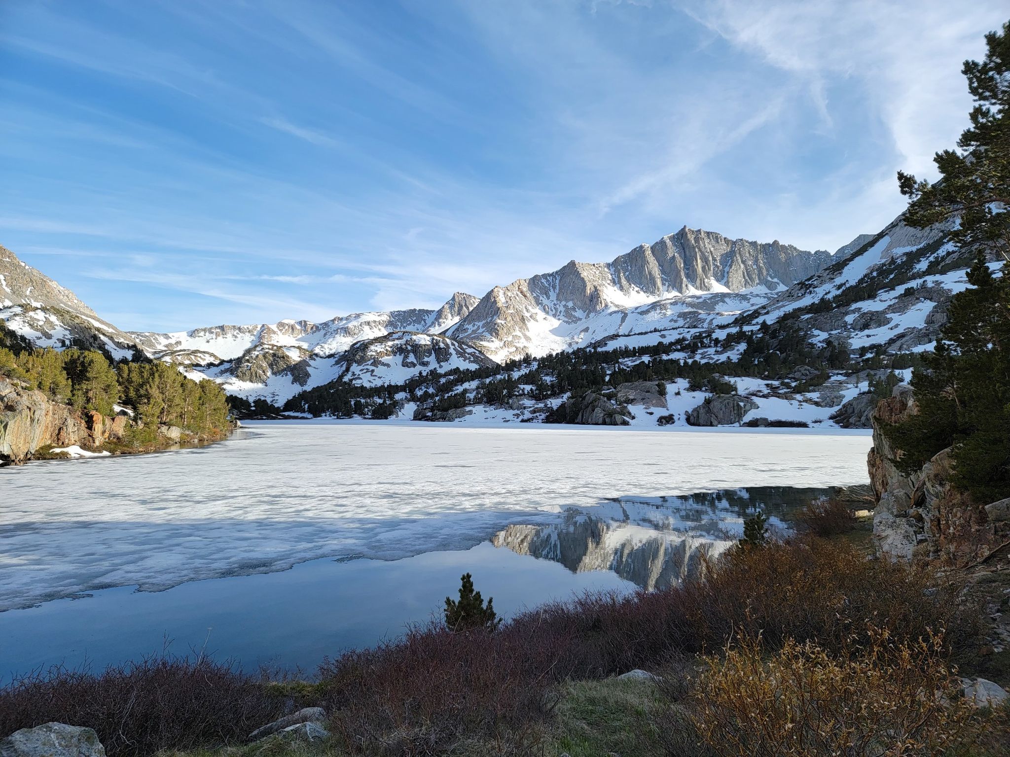 Partially frozen lake reflecting snowy mountains under a blue sky. - Chocolate Lakes loop