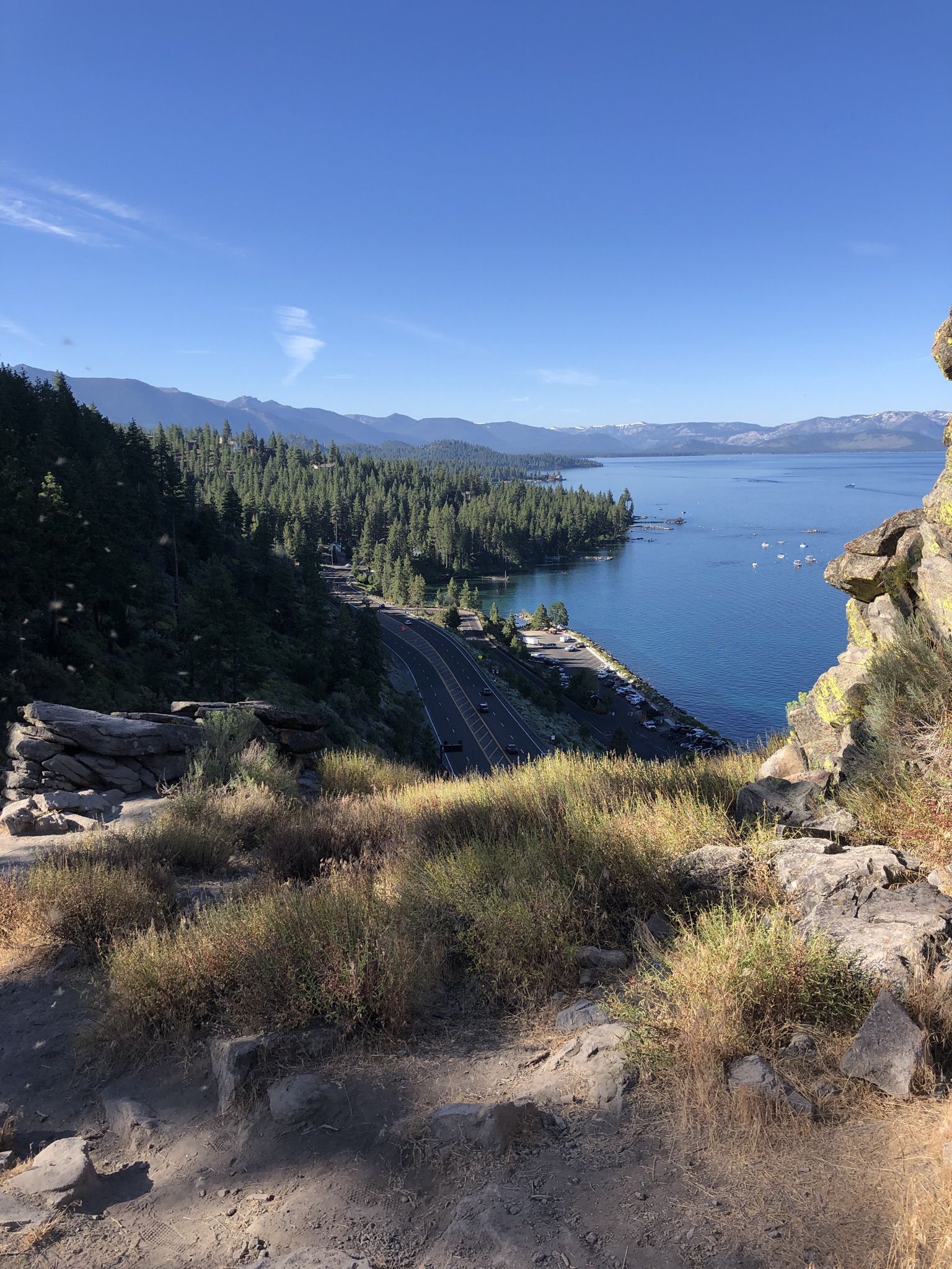 Elevated view of a winding road along a blue lake and dense green forests. - Cave Rock Overlook