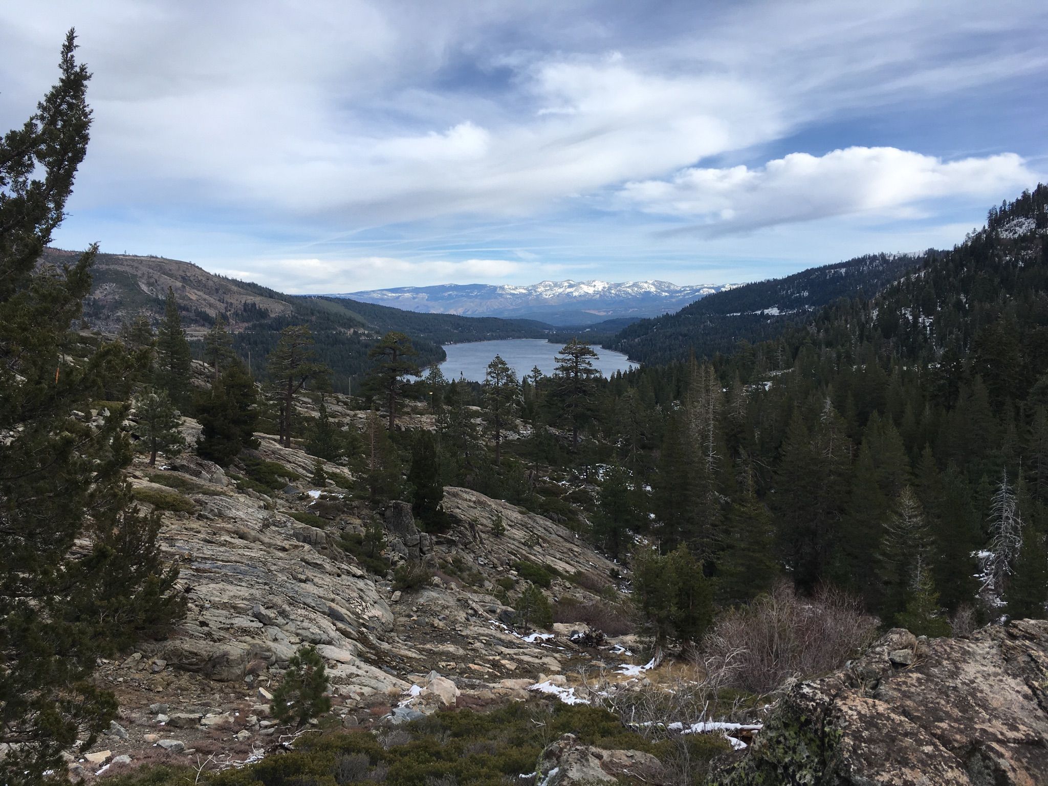 Panoramic view of a lake nestled among mountains with snow and pine trees. - Donner Summit Canyon