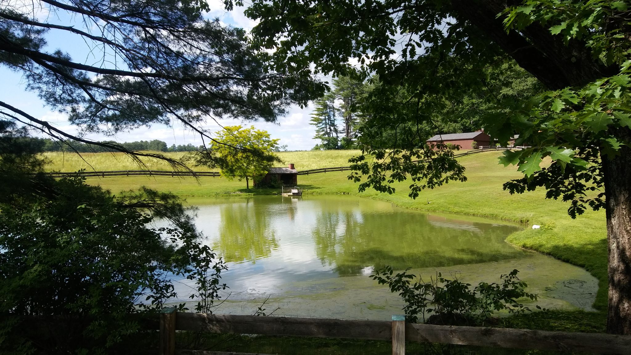 A sunny view of a pond with a small building and green fields. - Cochecho Falls (Cocheco Falls) – Vaughan Woods State Park loop from Dover