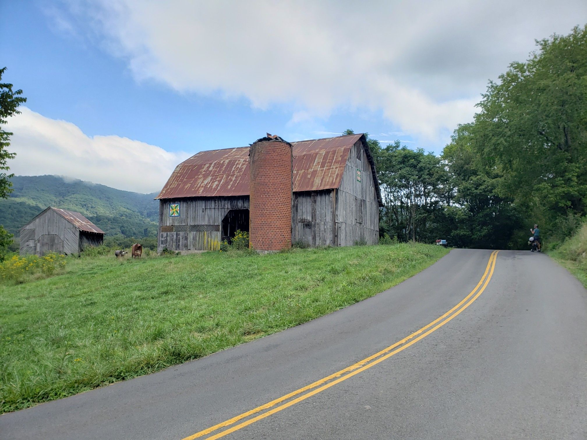Old wooden barn with silo, paved road, and forested hills under bright sky. - Roanoke City Market – Memorial Bridge loop from Roanoke
