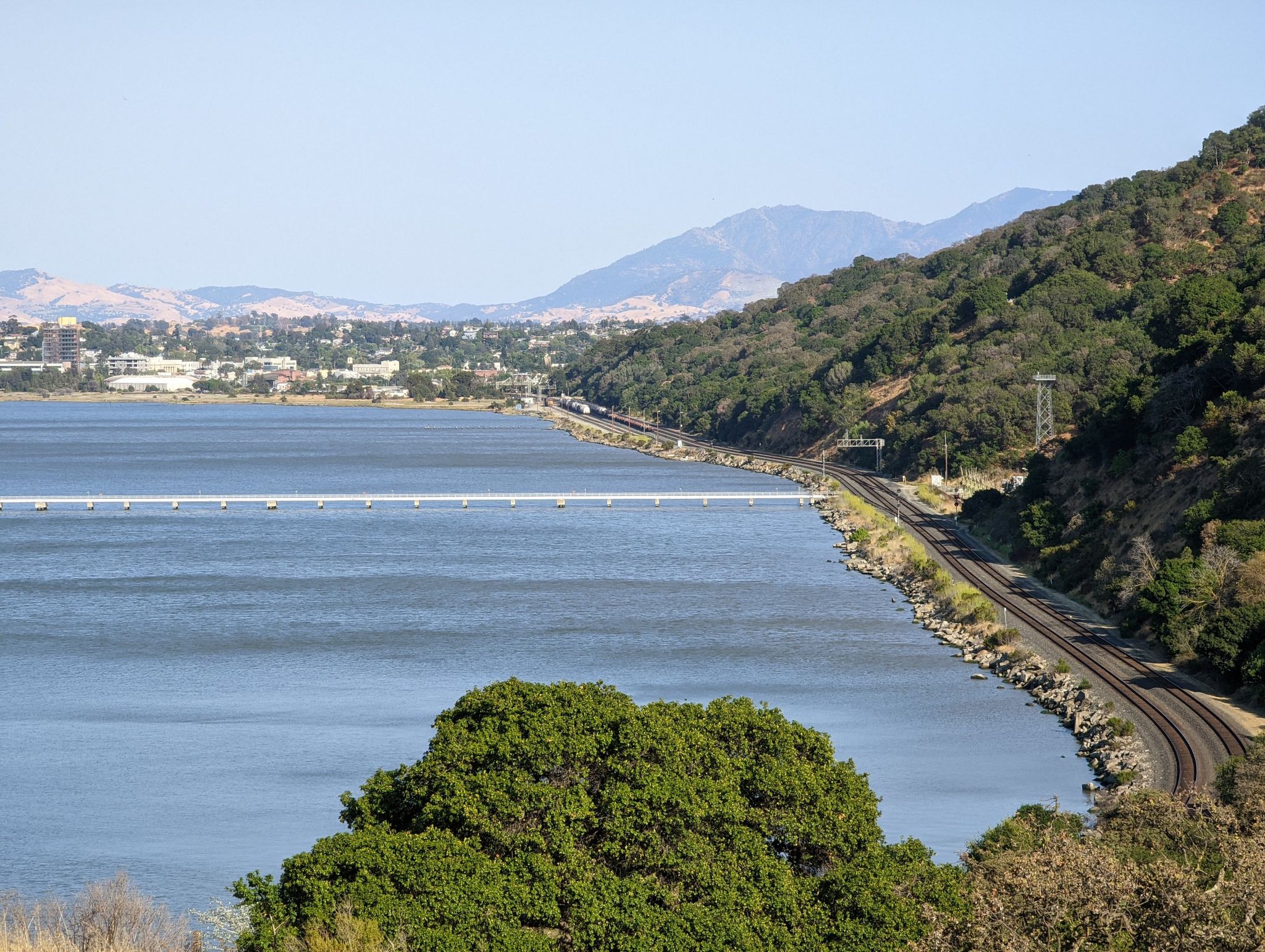 Expansive view of a bay, bridge, train tracks, and lush green hills. - Carquinez Scenic Drive through – Carquinez Bridge loop from Martinez