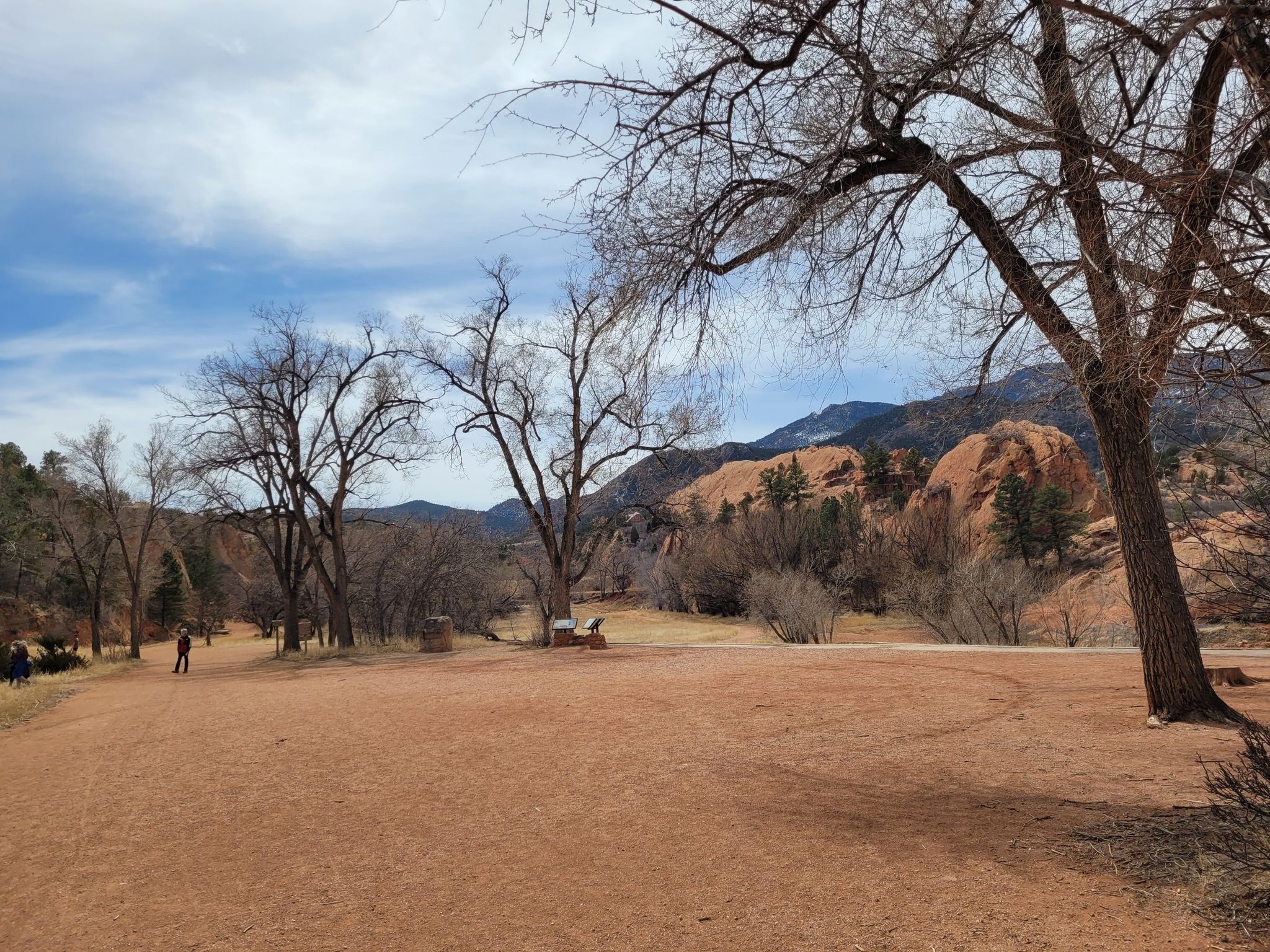 Open dirt area with bare trees, distant red rocks, and a person. - Sand Canyon, Greenlee, and Mesa Trail Loop