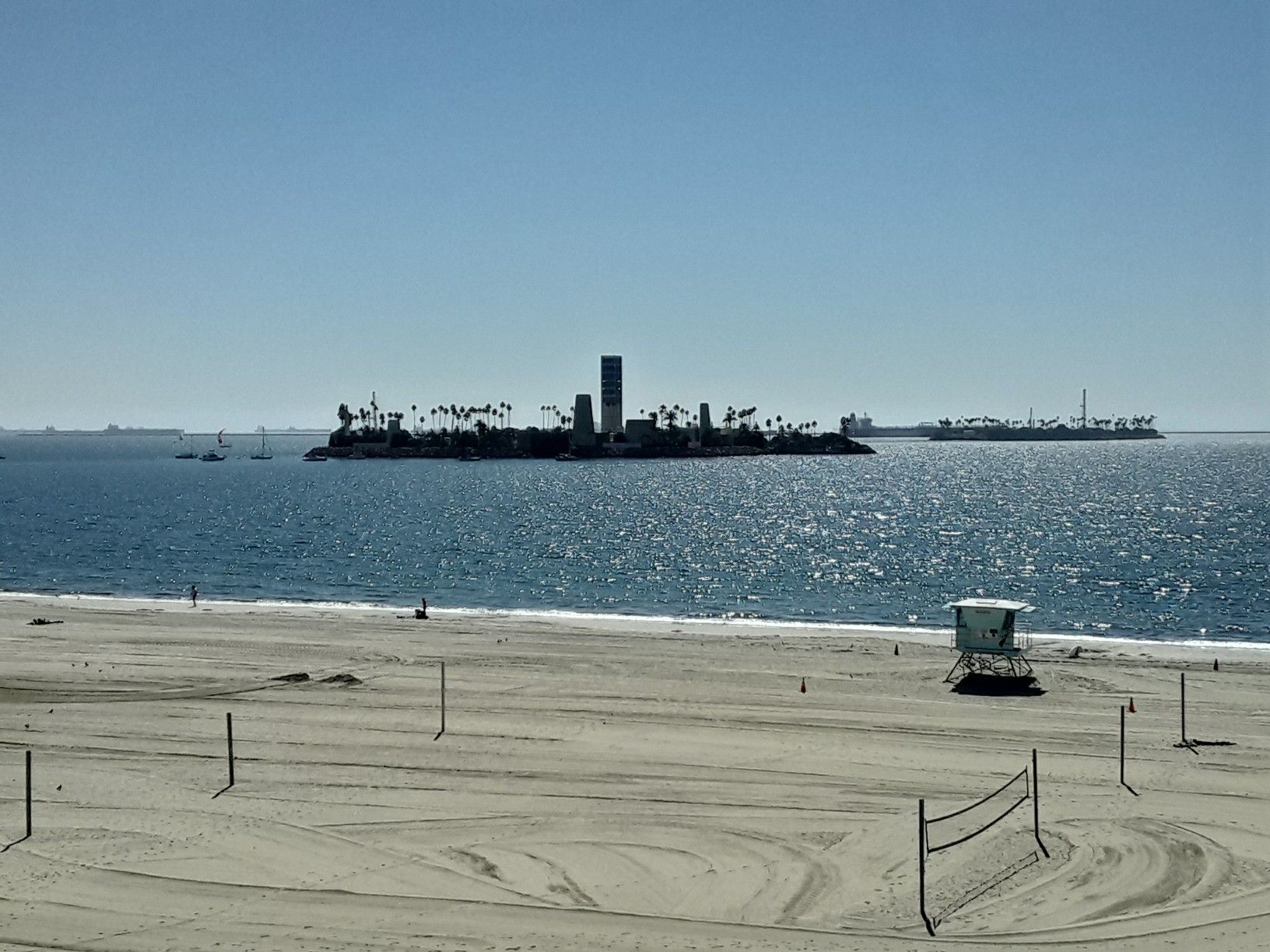 Sandy beach with volleyball nets, ocean, and distant artificial islands. - Bluff Park Loop