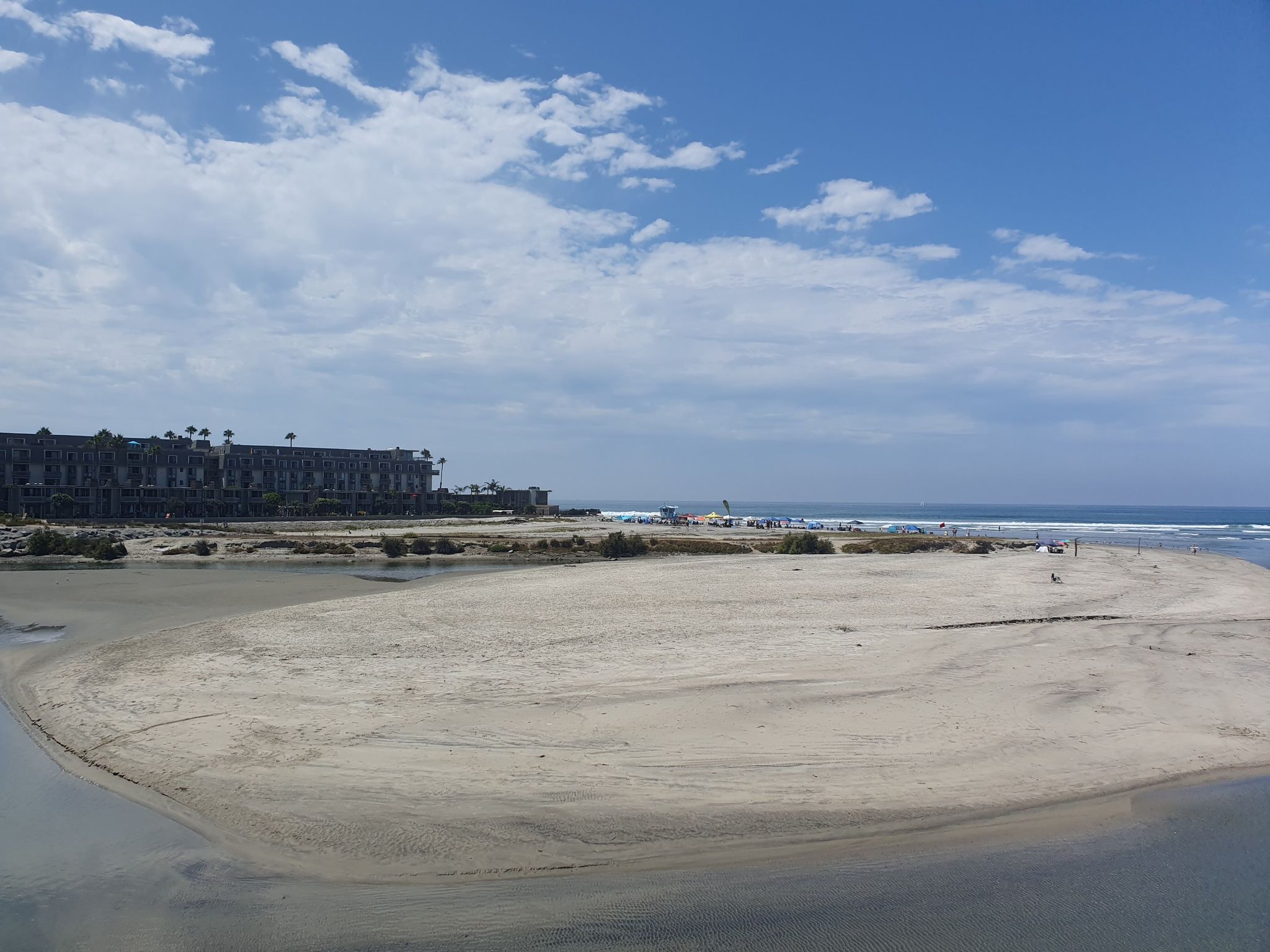 Expansive sandy beach meeting the ocean, with distant buildings under a cloudy sky. - San Luis Rey River – Oceanside Beach and Pier loop from Crouch Street