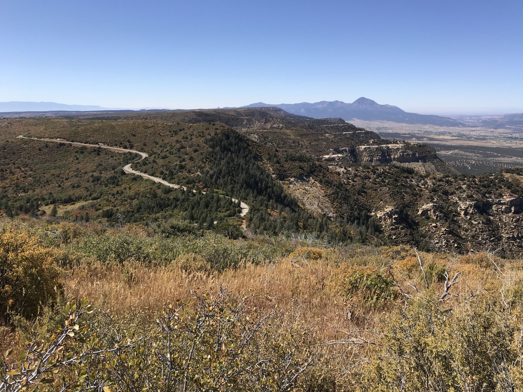 A winding road descends a forested mountain under a clear blue sky. - Park Point Trail