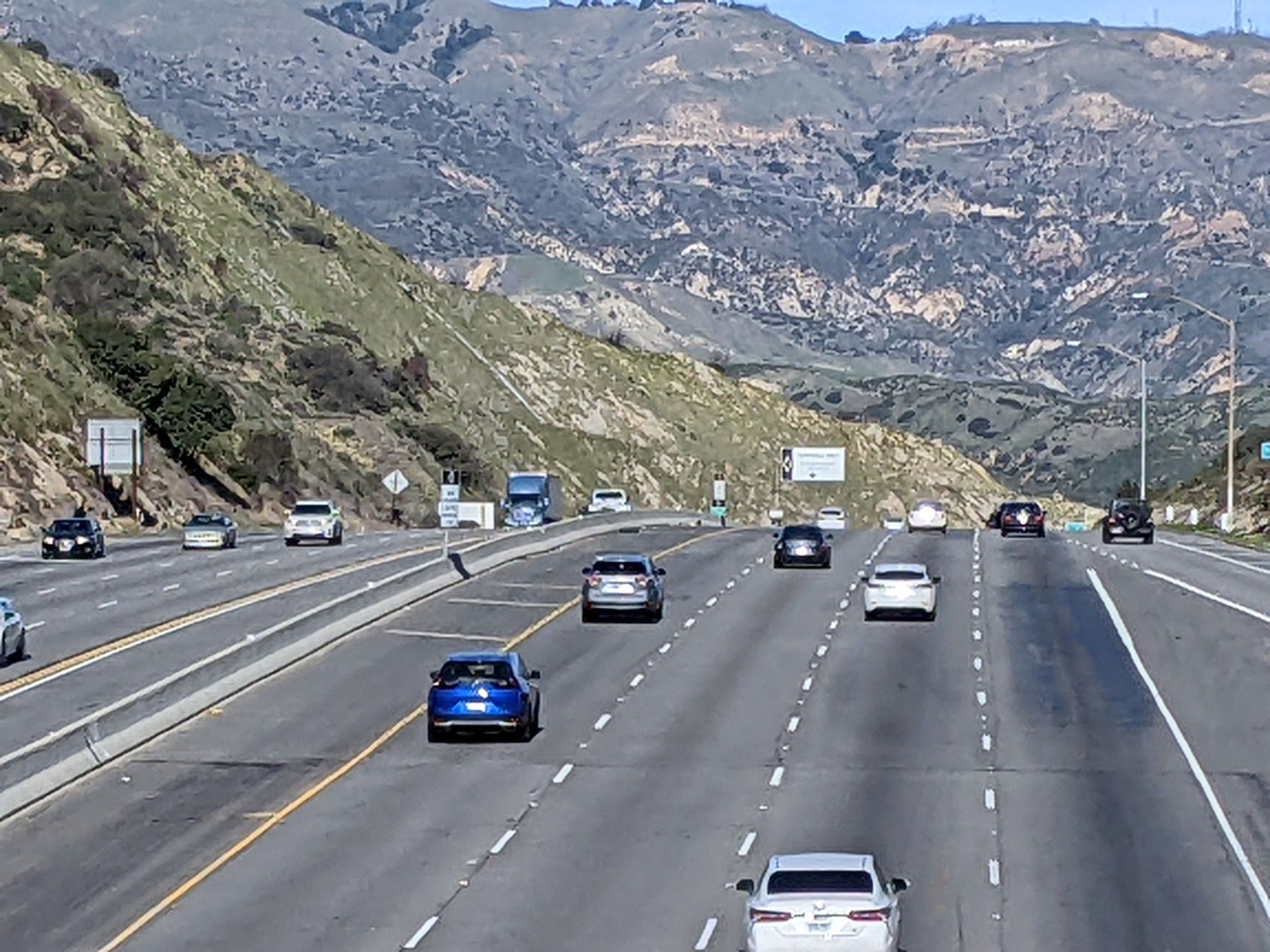 Cars on a multi-lane highway through green mountains under a clear sky. - Wildlife Corridor Trail