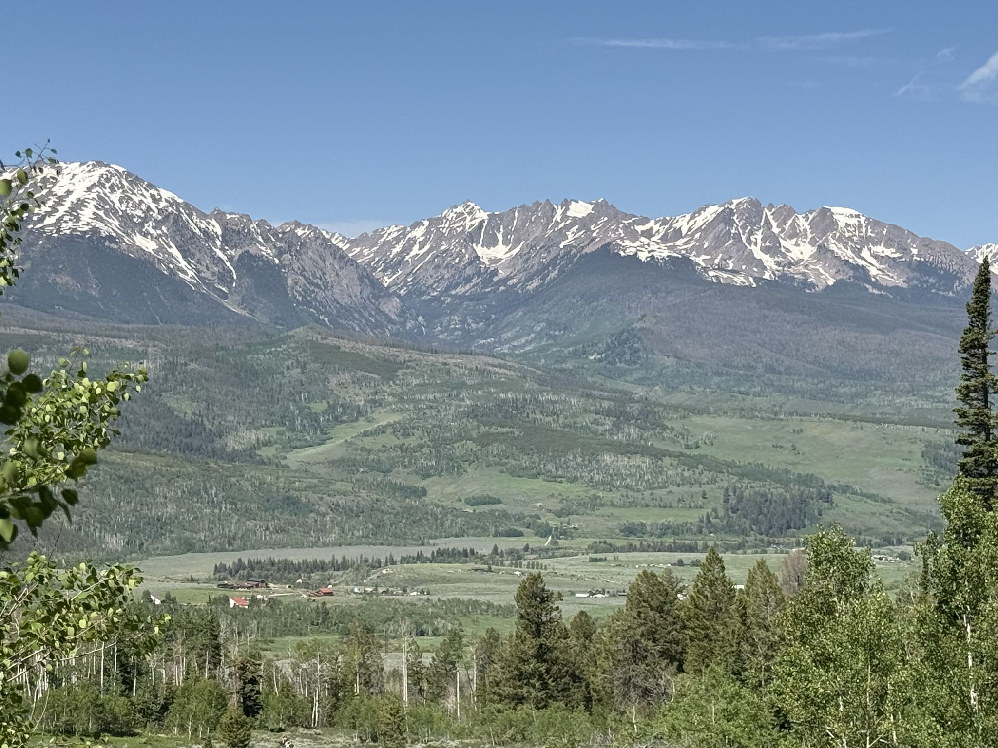 Bright day over snow-capped mountains, green valley, and distant settlement. - Ute Peak via Acorn Creek Trail