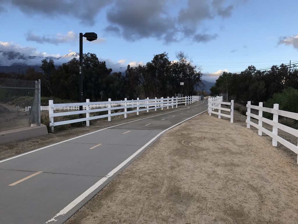 Paved path with white fences under a cloudy sky, mountains in the distance. - Pacific Electric Trail loop from Upland