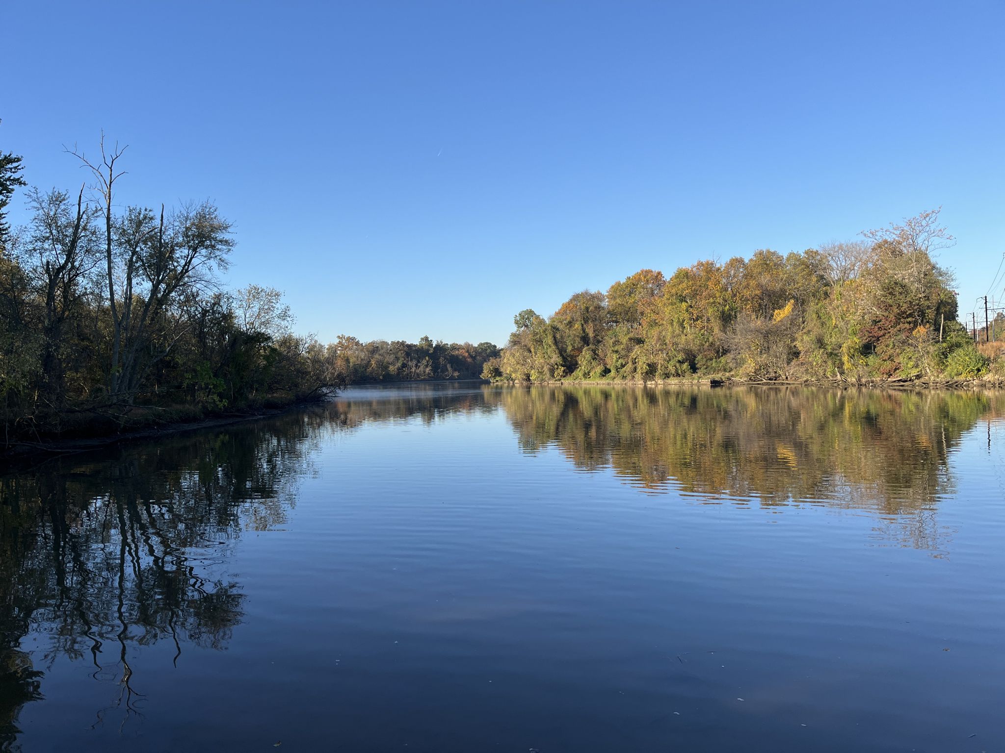 Calm river reflecting autumn trees on both banks under a clear blue sky. - Anacostia Riverwalk Trail