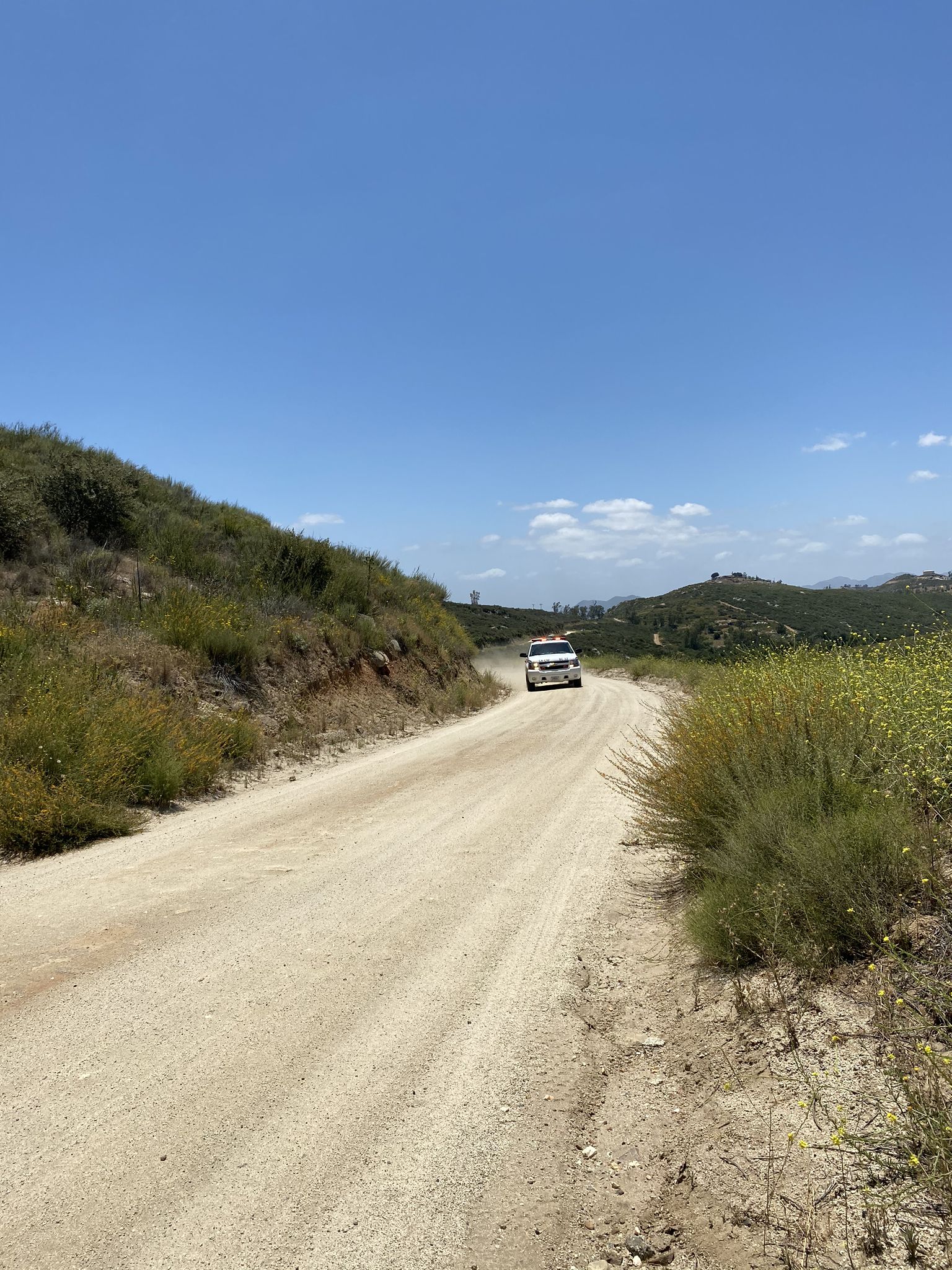 White vehicle on a sunny, winding dirt road through dry, green hills. - San Dieguito River loop from Ramona