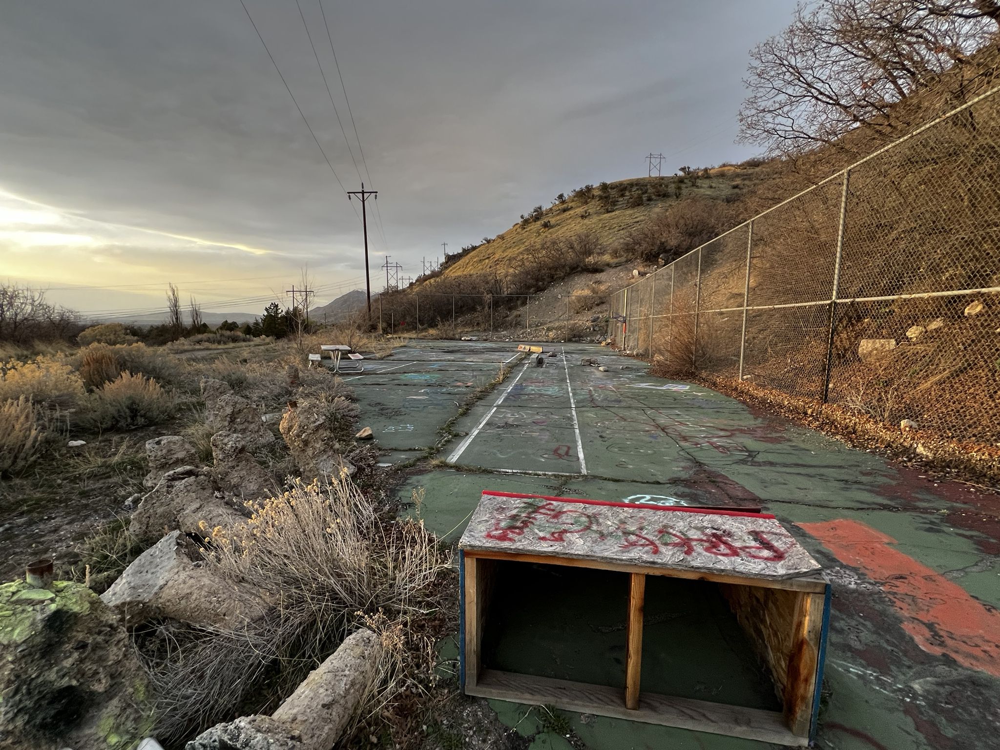 An abandoned, cracked tennis court with a wooden box under a cloudy sky. - Bonneville Shoreline Trail: Rock Canyon Park Connector