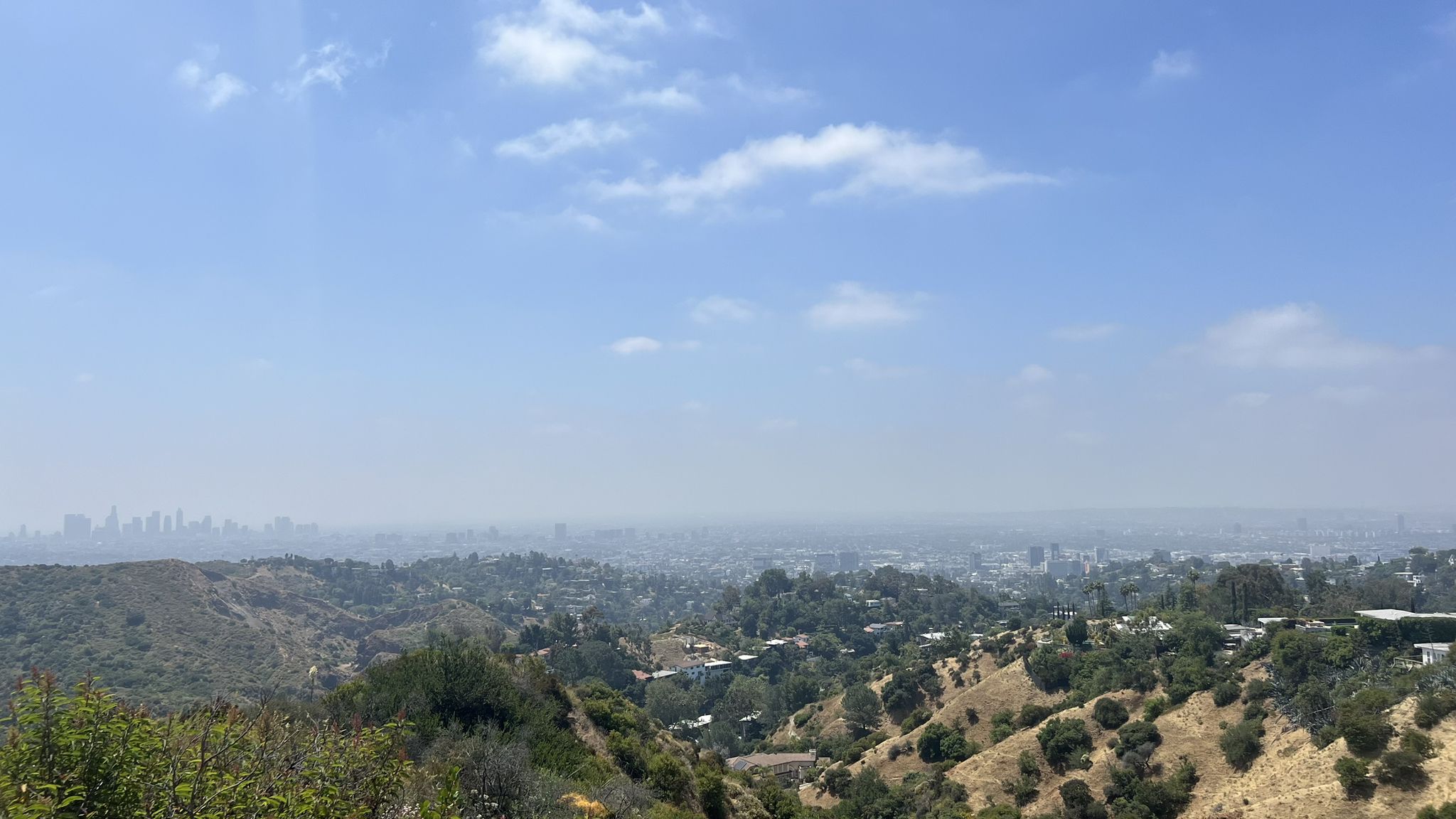 Hazy panoramic view of a city sprawling across hills under a cloudy sky. - Hollywood Sign via Brush Canyon and Mulholland Trails