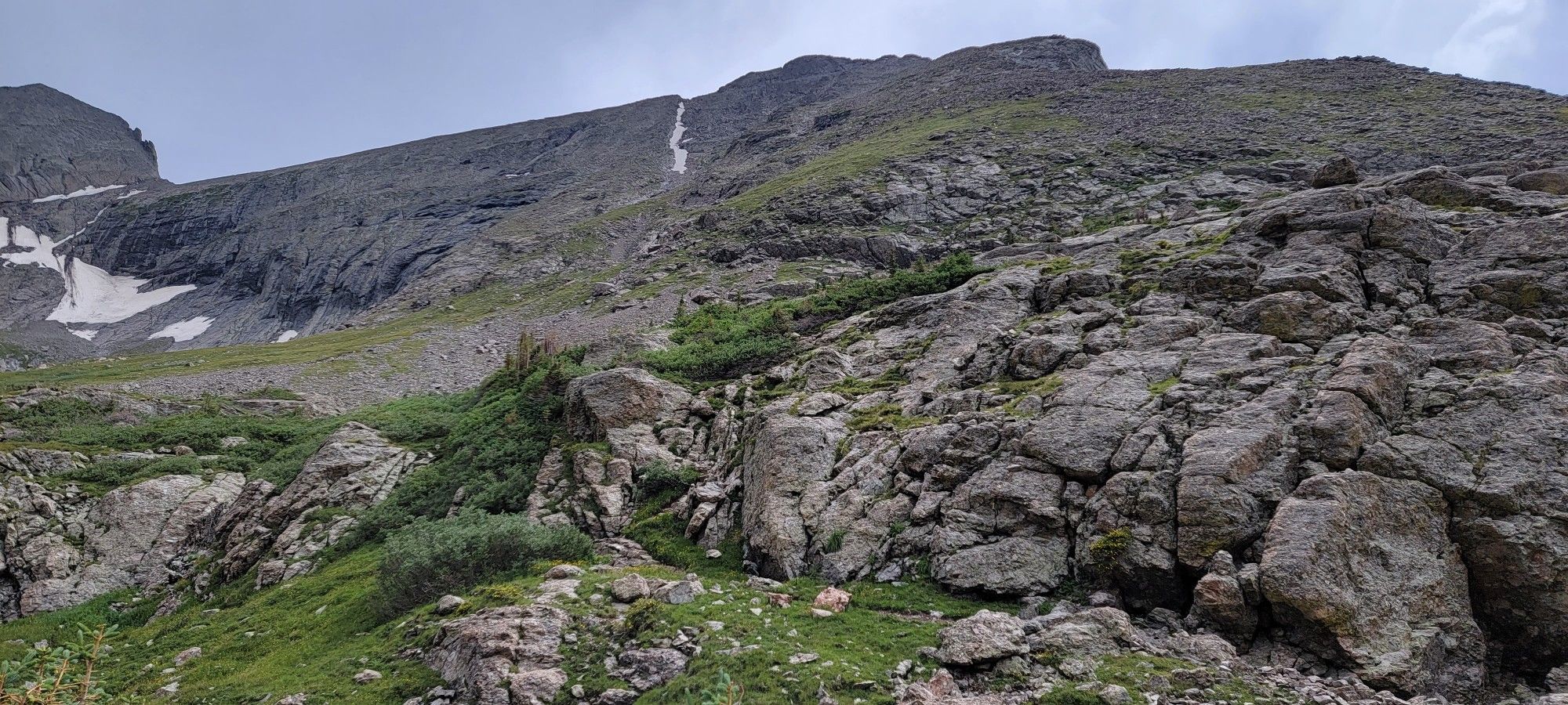 Steep, rocky mountain slope with patches of green and snow under cloudy sky. - Kit Carson Mountain & Challenger Point via Willow Lake