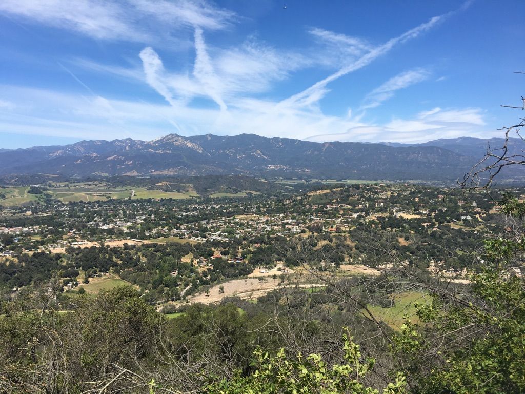 Expansive view of a town nestled among green hills and distant mountains. - Ojai loop