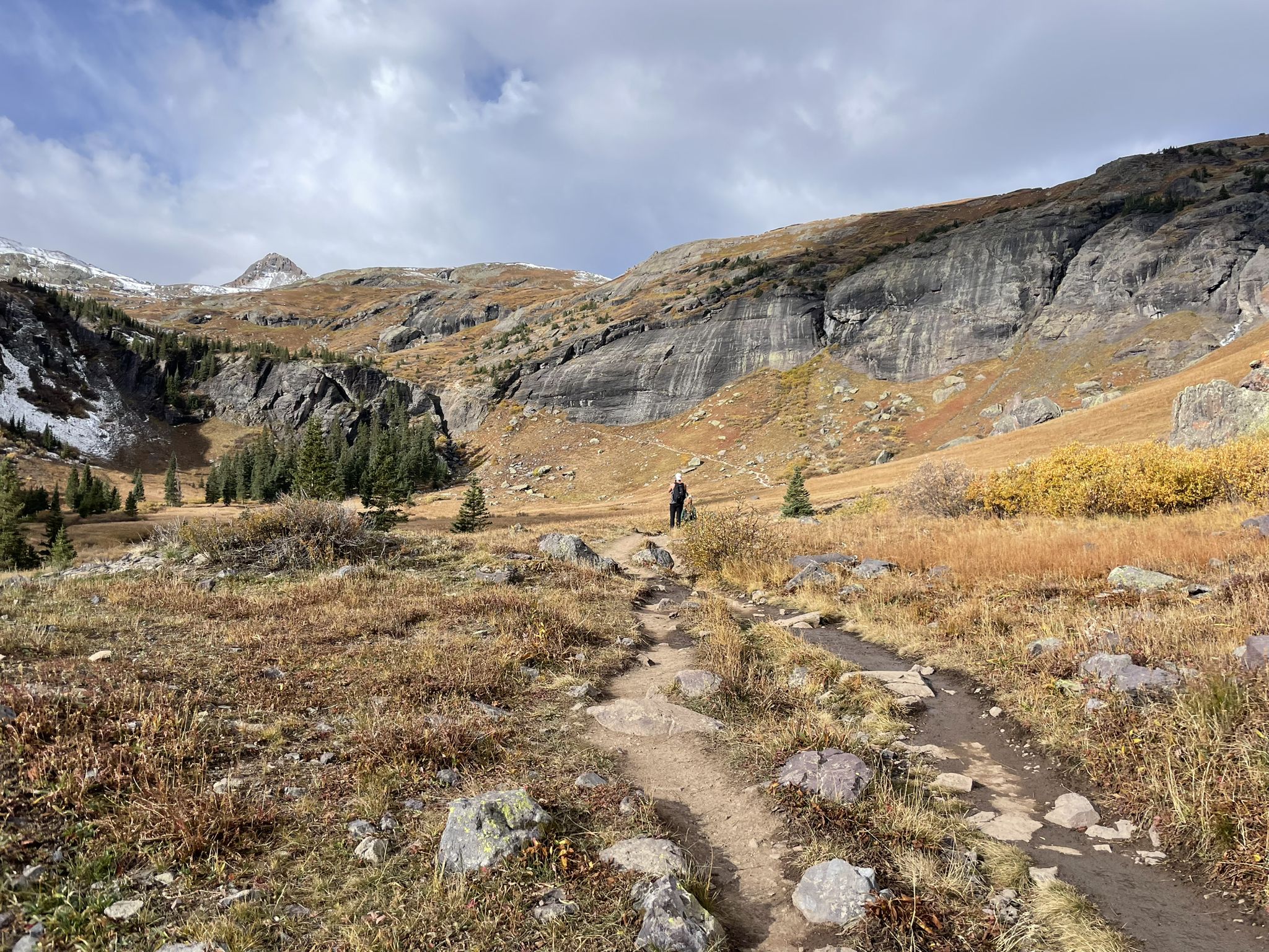 Hiker on a dirt path in a vast, cloudy mountain valley. - Ice Lakes Trail