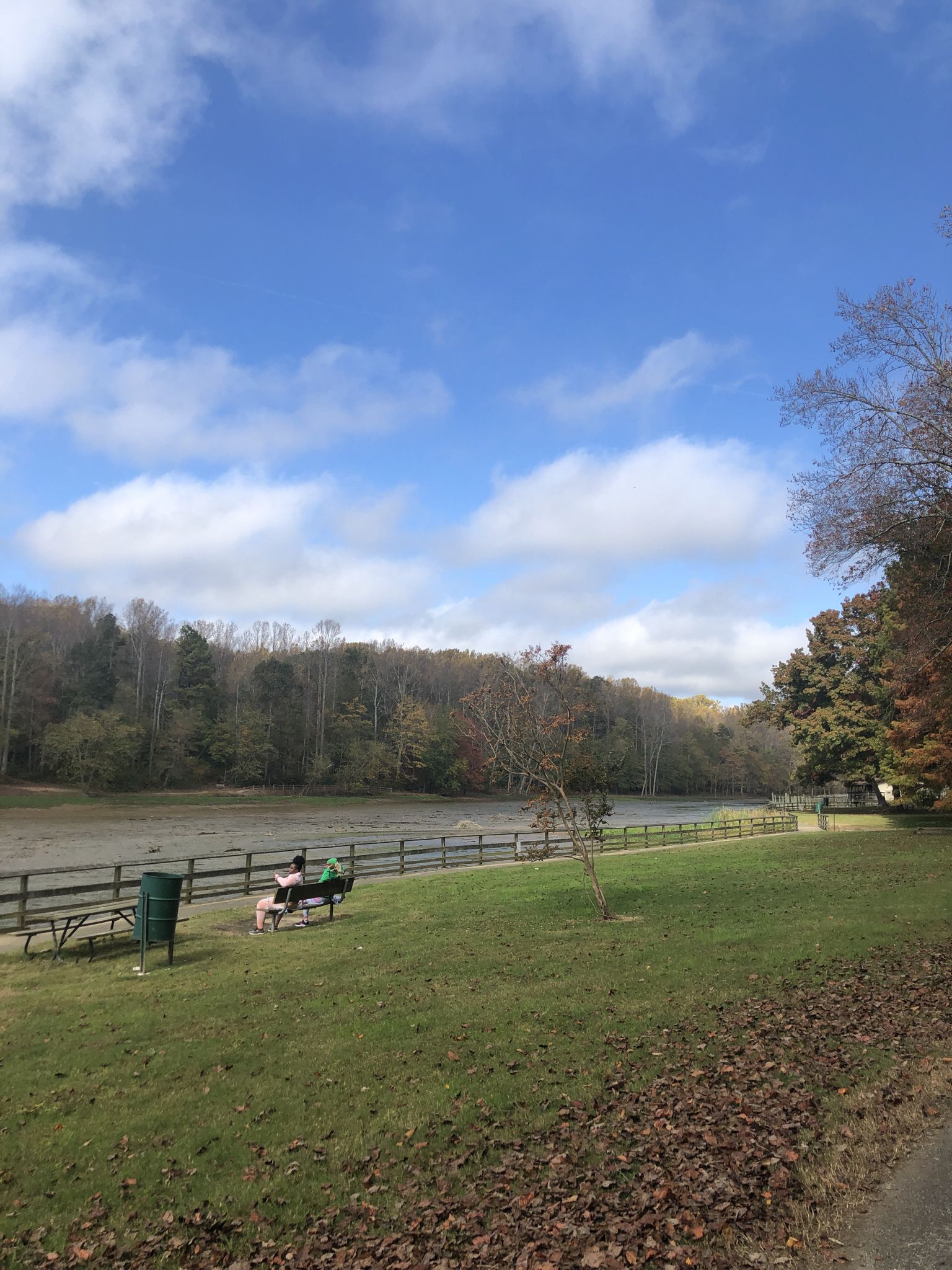 People sit by a dry lakebed, surrounded by autumn trees under a blue sky. - Cosca Regional Park Green Loop