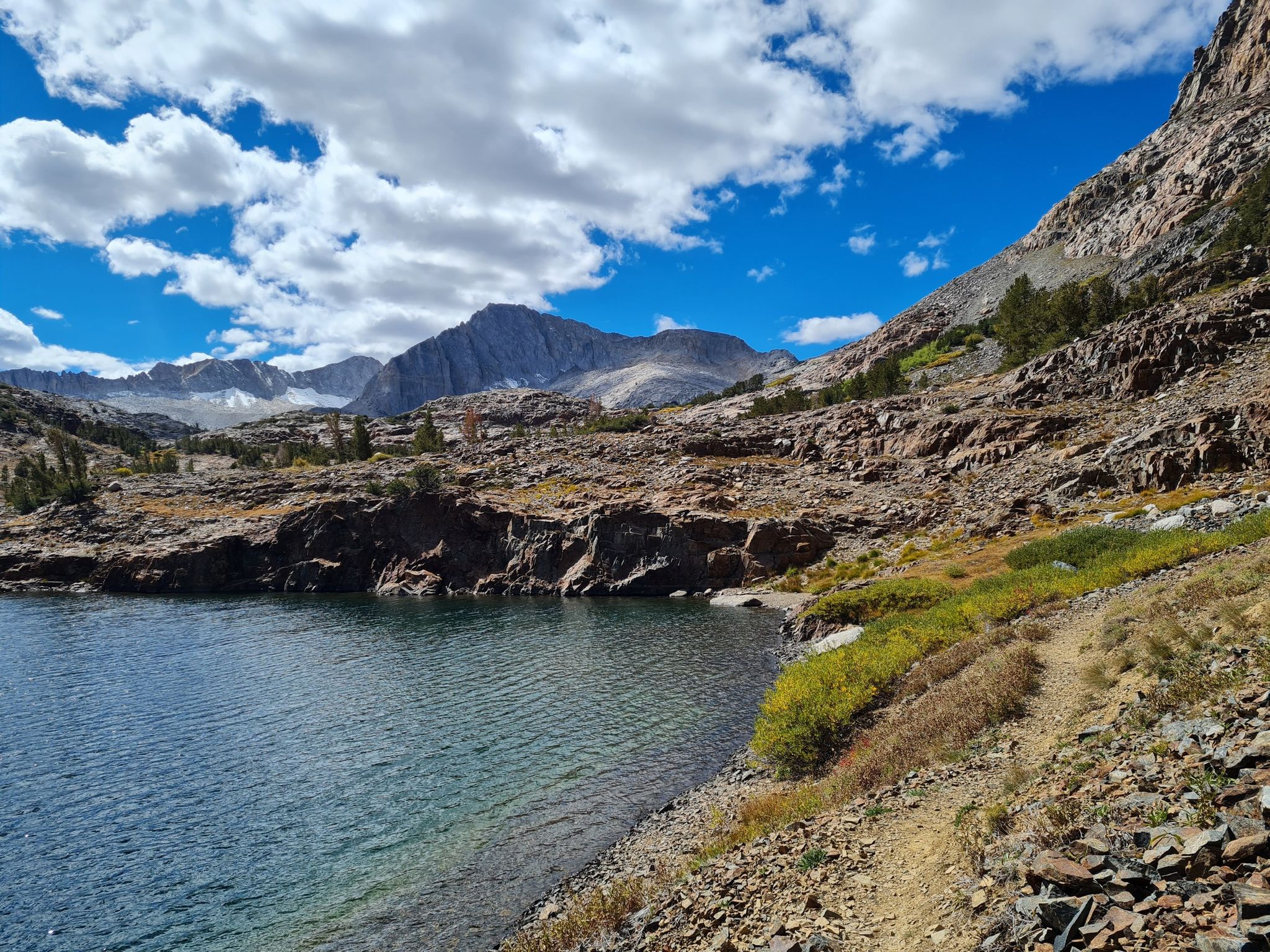 Clear mountain lake with rocky shore under a bright blue sky. - Twenty Lakes Basin and Saddlebag Lake Loop