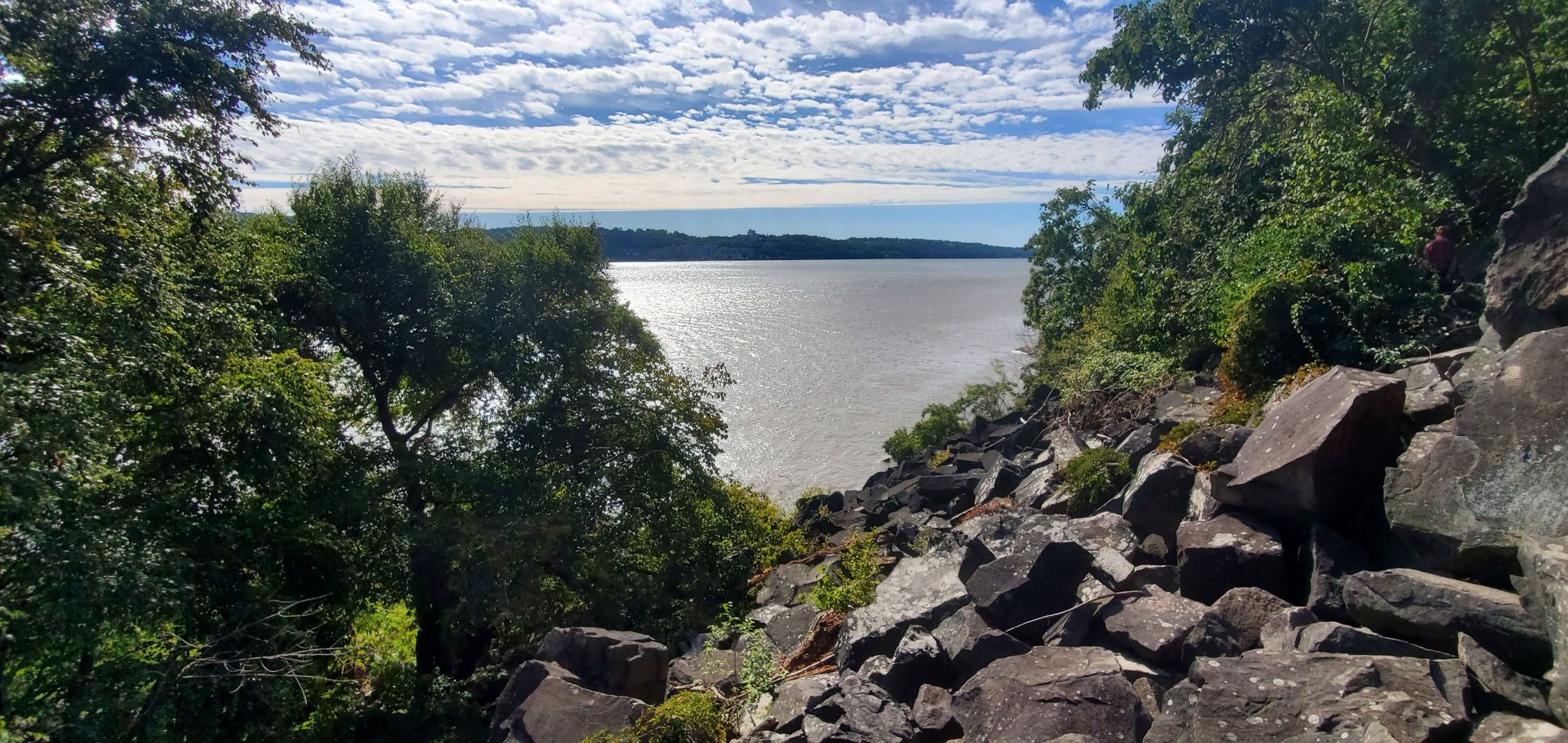 Rocky shoreline and green trees beside a wide, sparkling body of water. - Long Path and Shore Trail Loop