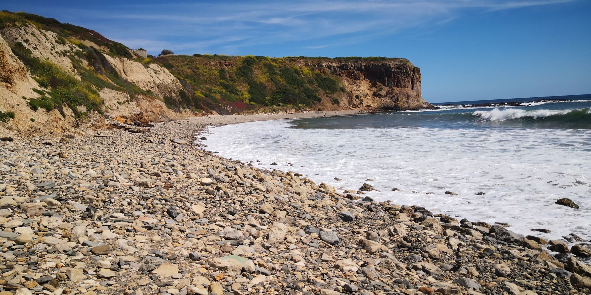Rocky beach with crashing waves and steep cliffs under a bright sky. - Portuguese Point Loop Trail