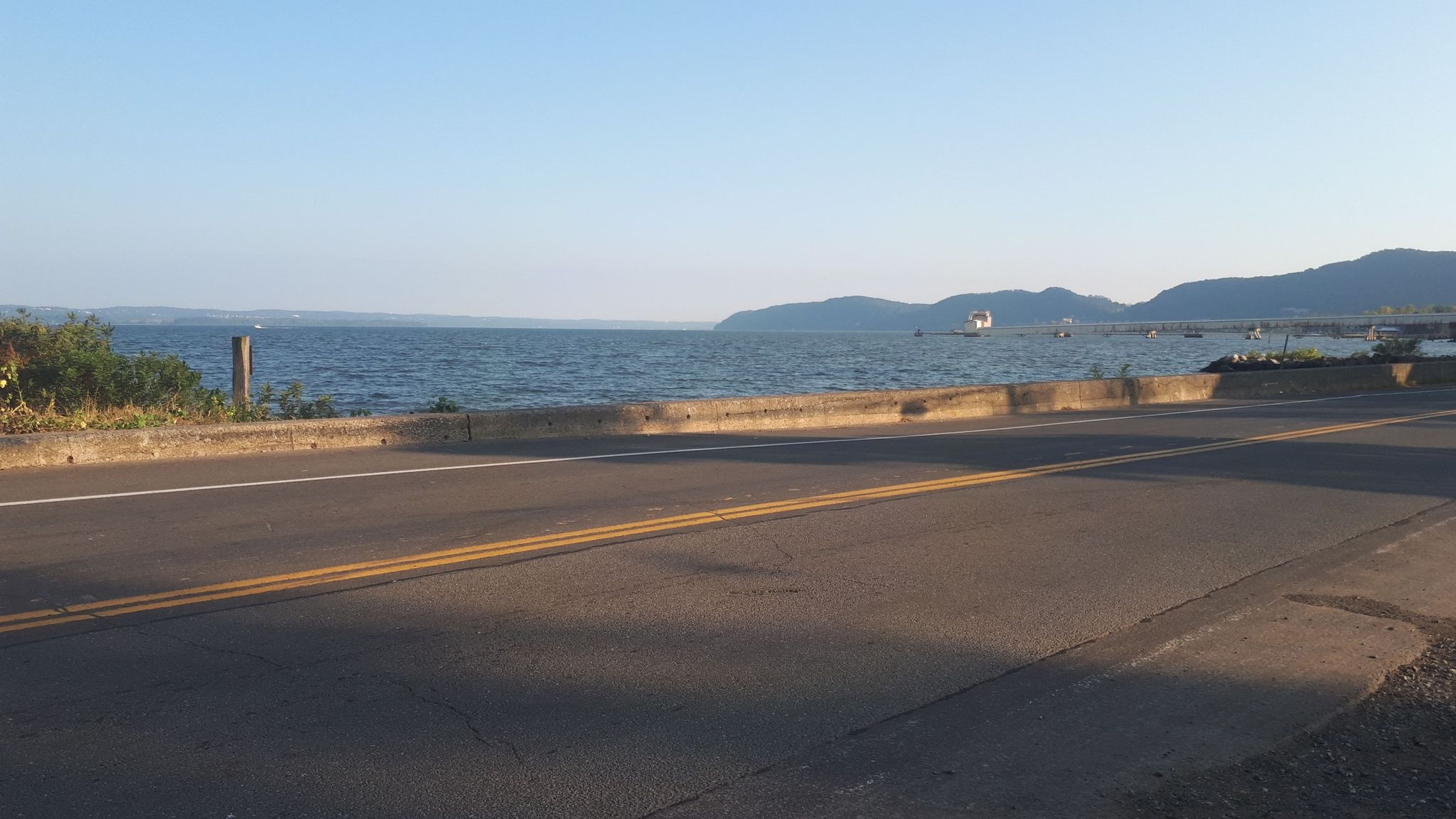 Road alongside a vast body of water with distant mountains under a clear sky. - East of the Orchards – Orchards of Conklin loop from Mount Ivy