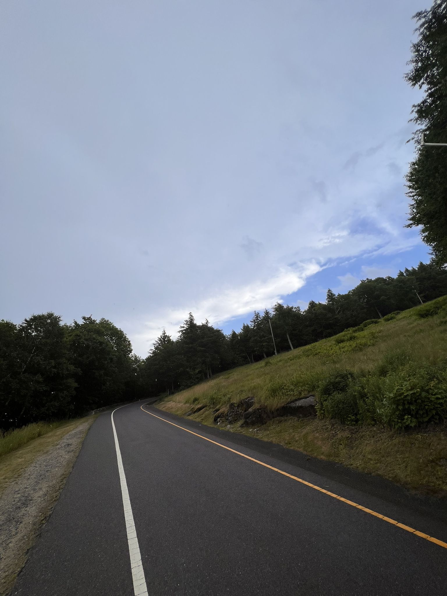 A paved road curves uphill beside a grassy slope under a dramatic sky. - Wachusett Mountain Lodge – Mount Wachusett loop from Redemption Rock