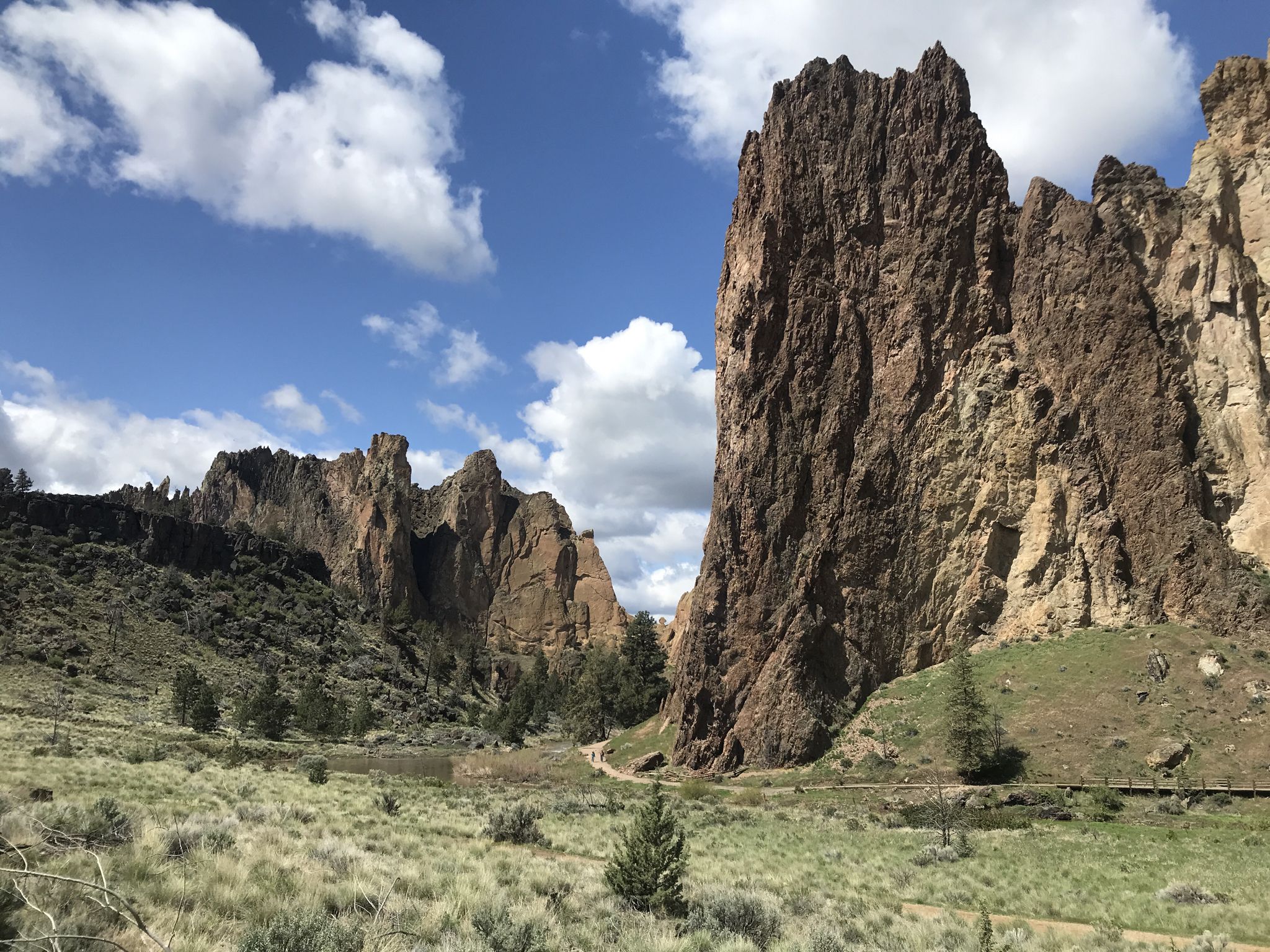 Towering rock formations rise from a green grassy valley under a cloudy sky. - View of Smith Rock State Park – Northern Point loop from Smith Rock State Park