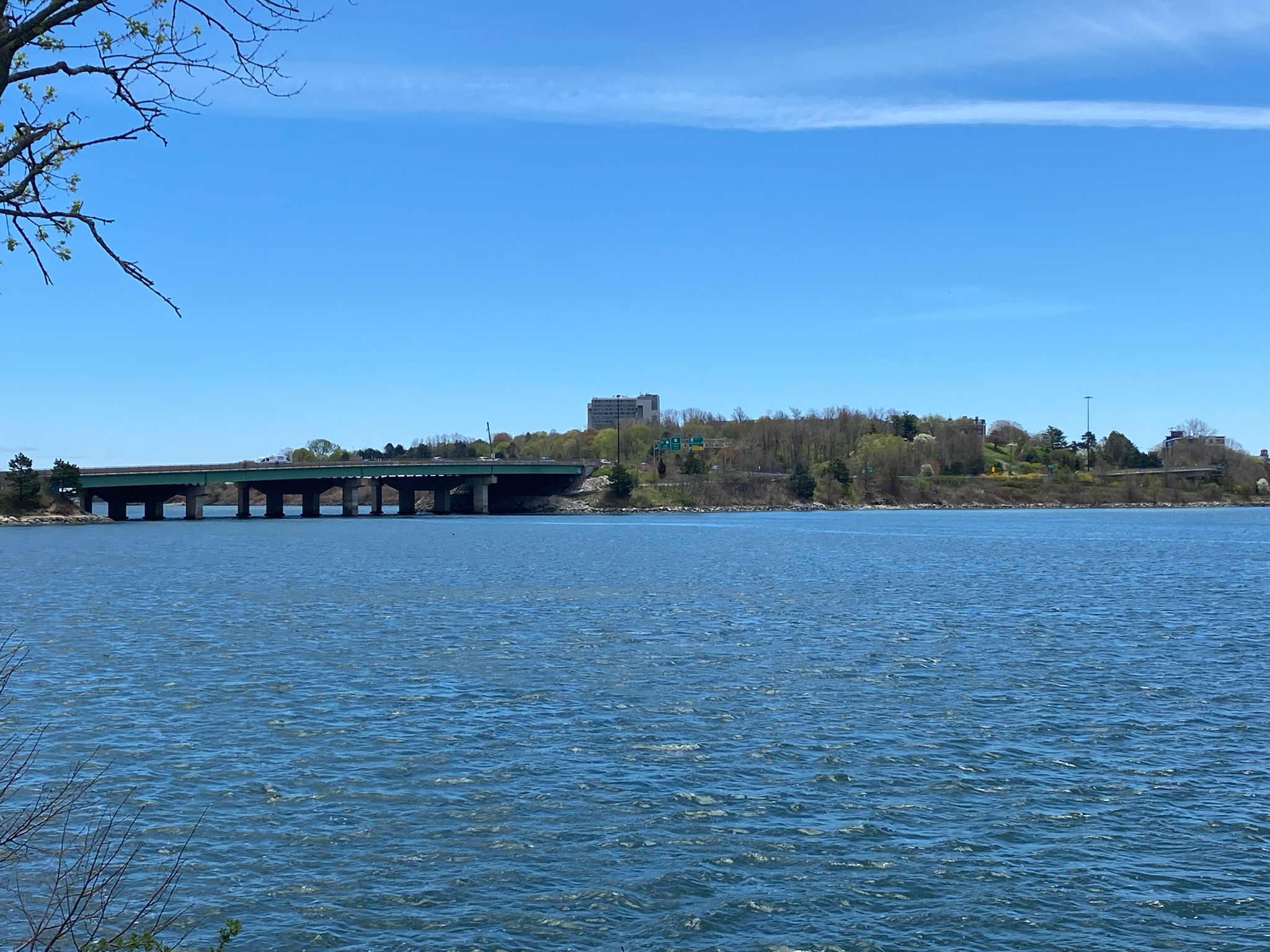 A wide body of water with a long bridge and distant buildings under a clear blue sky. - Eastern Promenade Trail – East End Beach loop from Portland