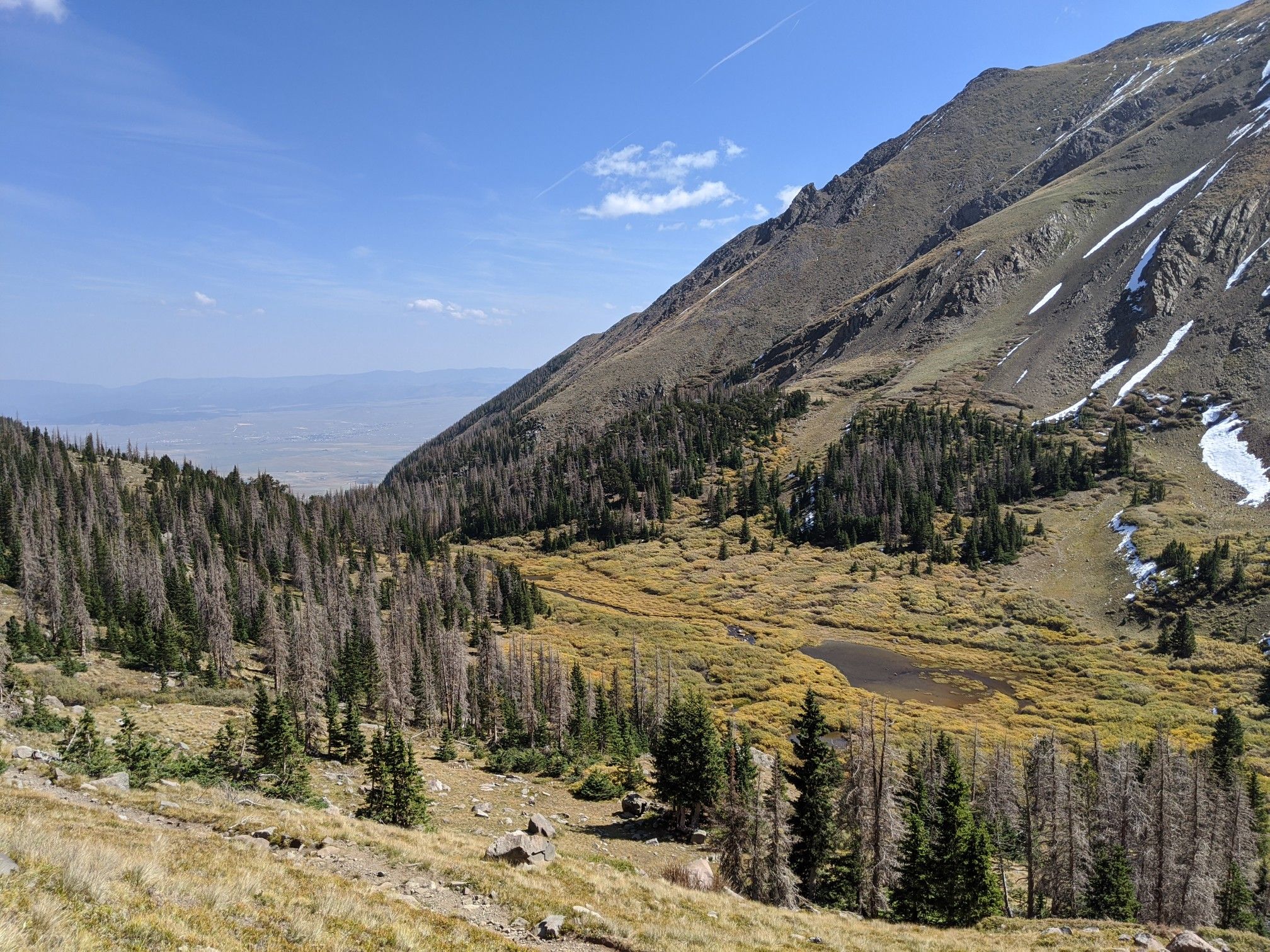 Mountain valley with pond, evergreen trees, and distant plains under blue sky. - Rito Alto four pass loop