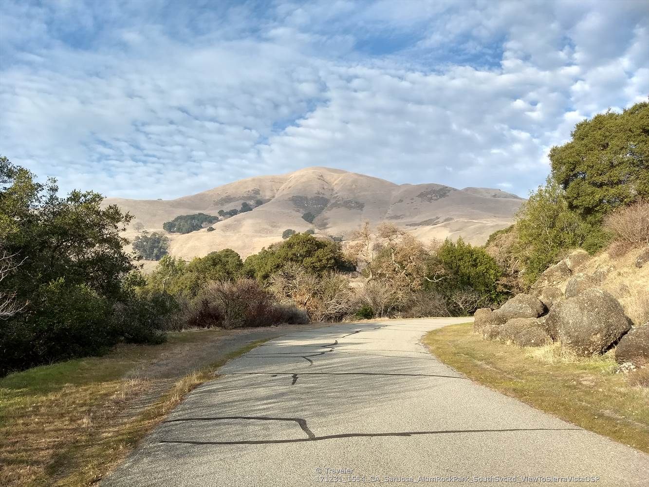 Paved road winding through green hills towards large mountains under a cloudy sky. - Upper Penitencia Creek – Inspiration Point loop from Alum Rock Park