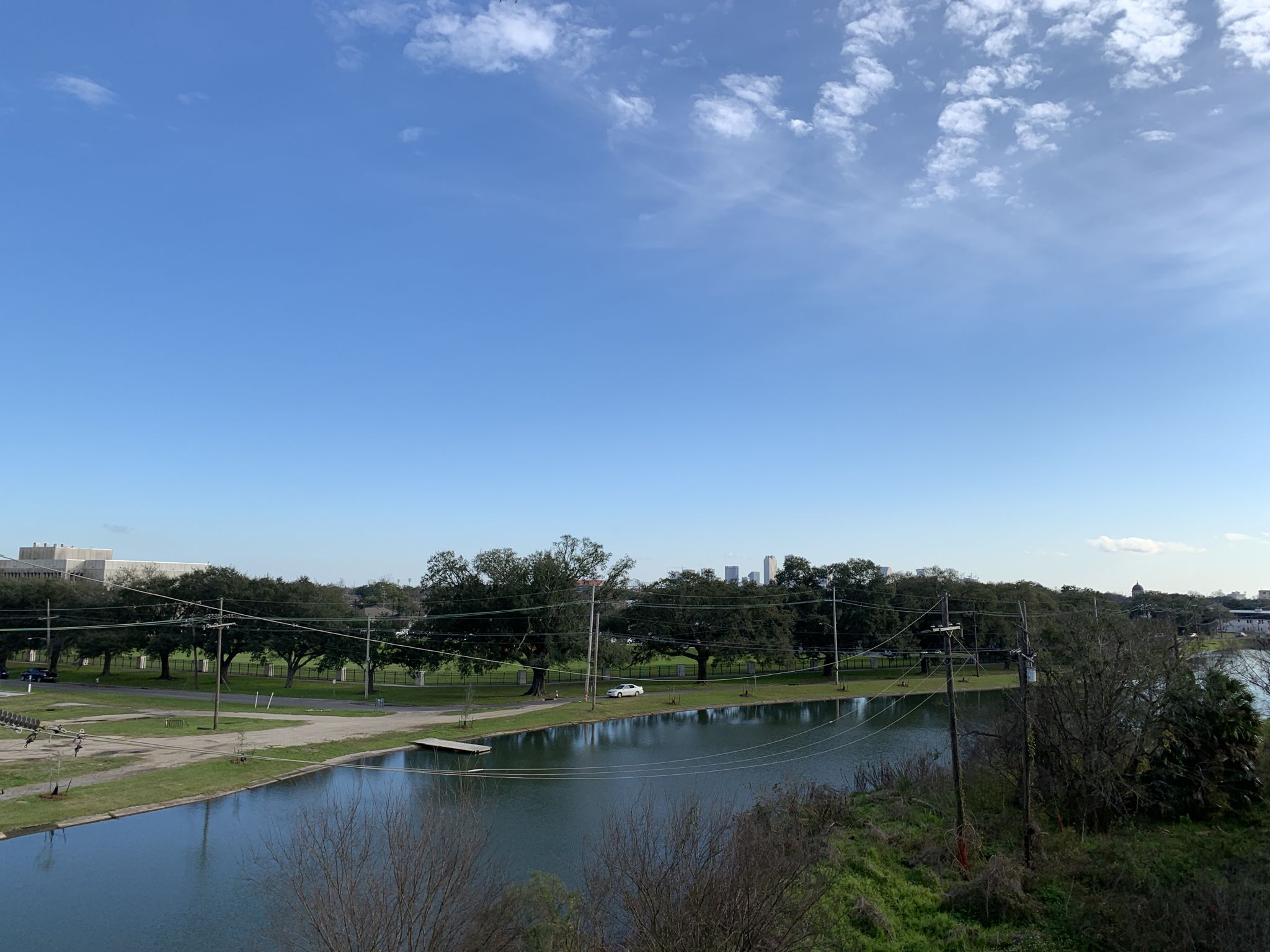 A wide waterway with trees and distant buildings under a bright blue sky. - New Orleans City Park South Loop
