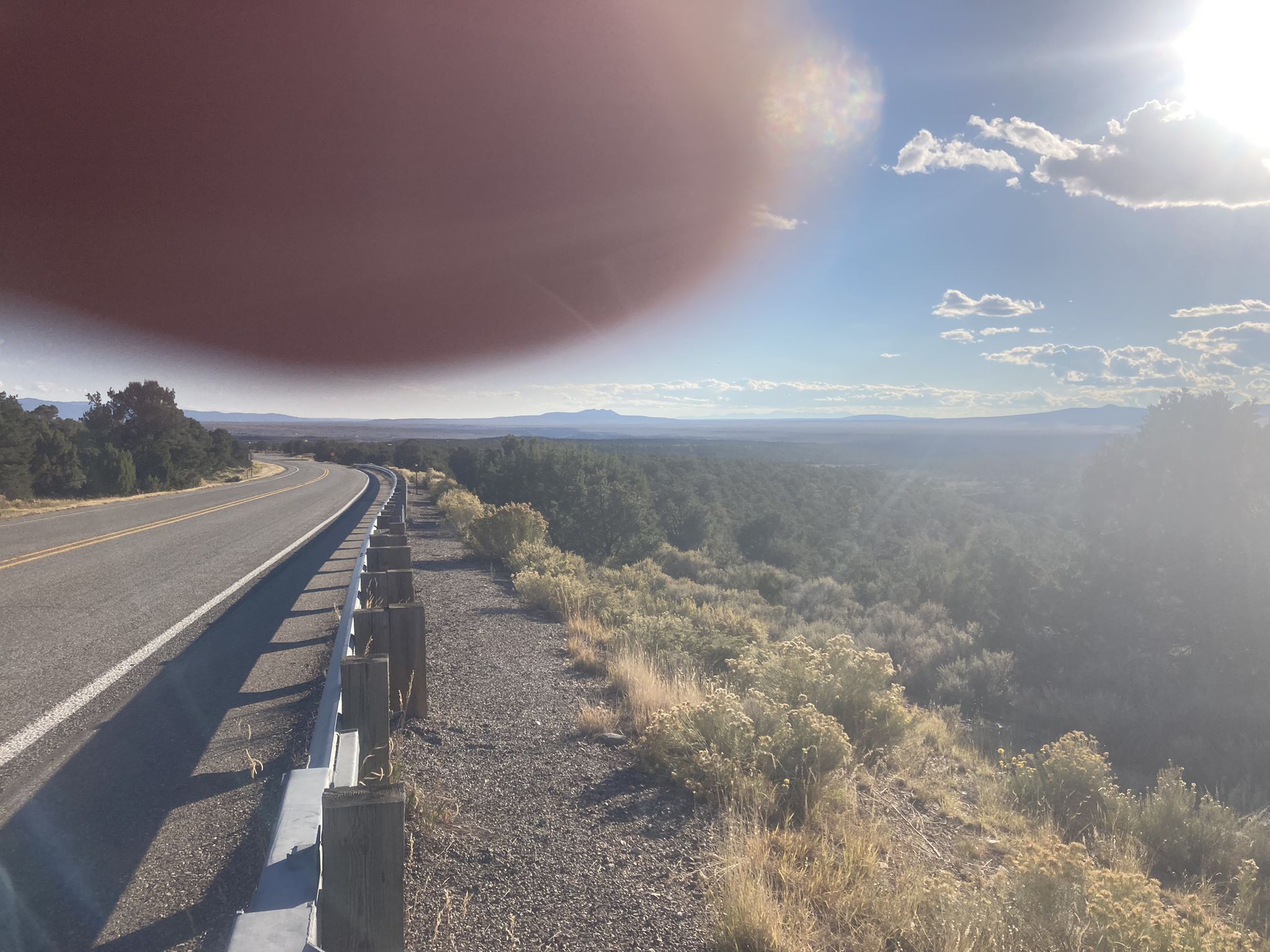 A winding road overlooks a vast, sunny, forested landscape with distant mountains. - Enchanted Circle