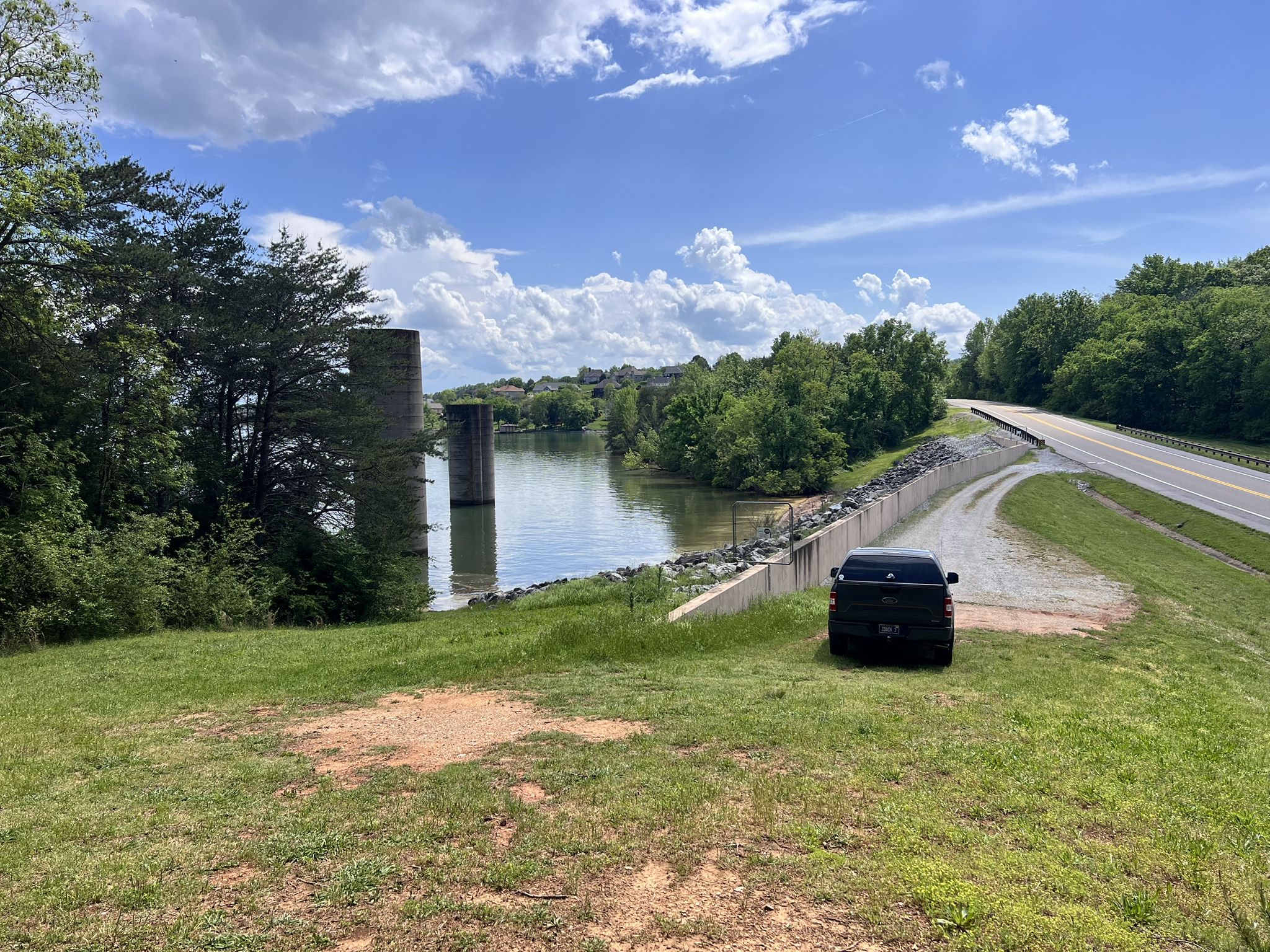 Black car parked on grassy bank overlooking river and bridge pillars. - Hall Bend Trail