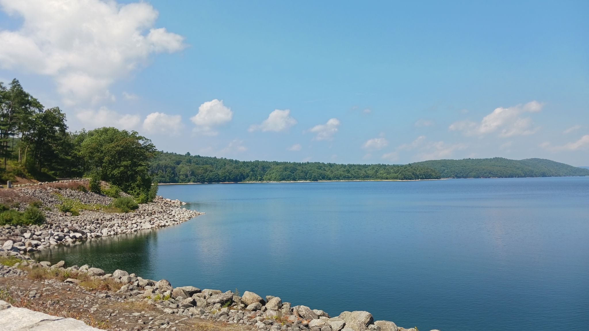 Calm blue lake with rocky shore and distant green hills under a bright sky. - Goodnough Dike Loop