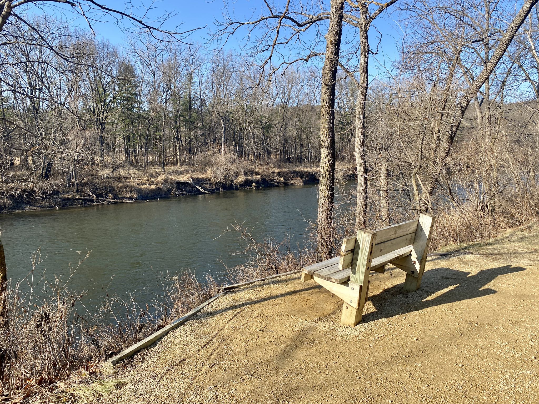 A wooden bench overlooks a river with bare trees under a clear sky. - One Lane Bridge – Cannon Valley Trail loop from Cannon Falls