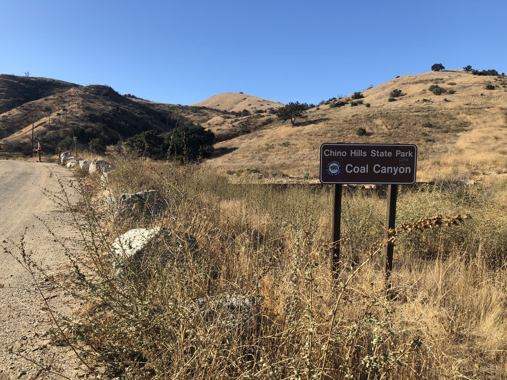 A park sign in a dry, grassy field with rolling hills under clear sky. - Sierra Peak Summit