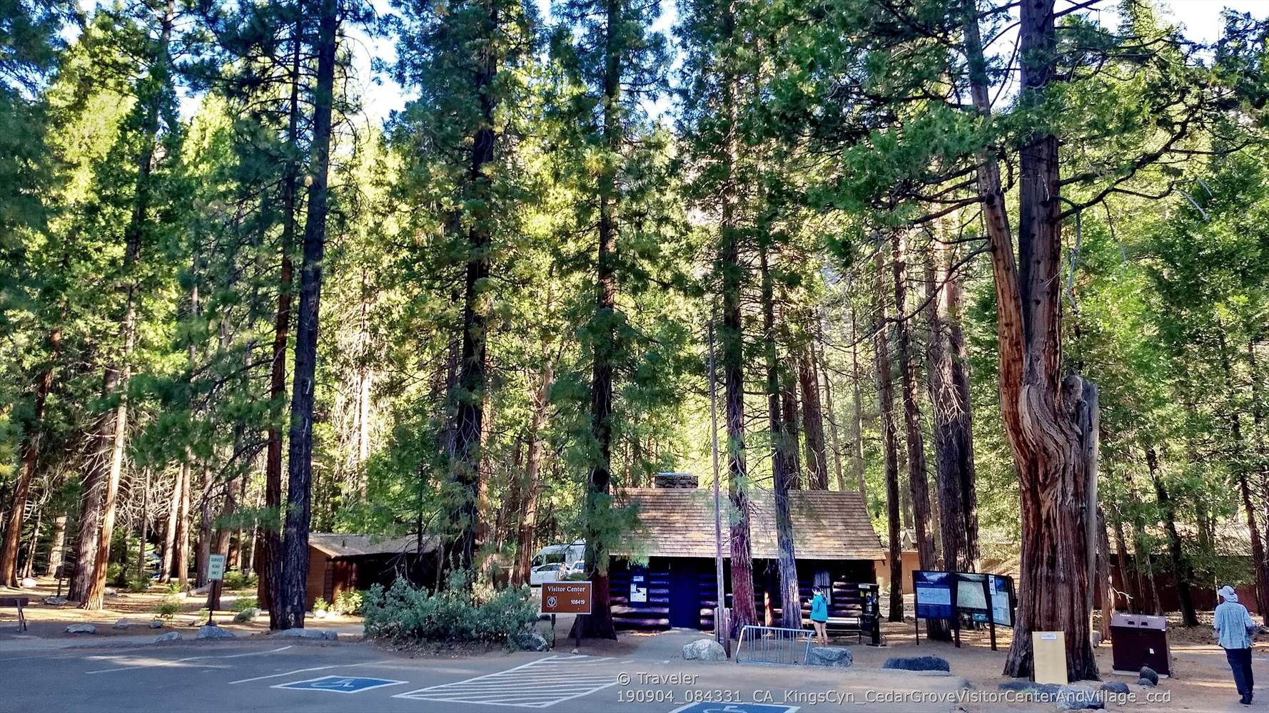 Tall pine trees surround a rustic building and parking lot with a few people. - Grizzly Falls to Road's End