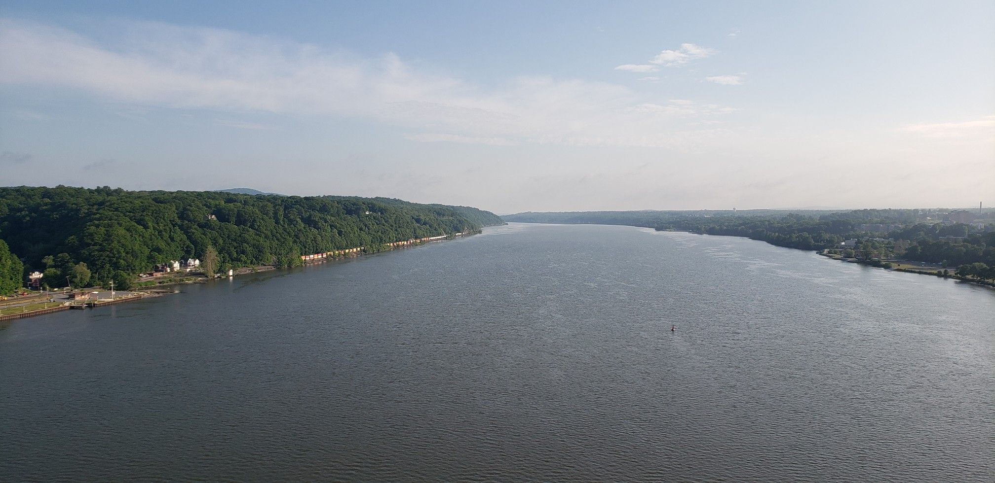 Wide river flowing between forested banks under a bright, hazy sky. - Walkway Over the Hudson – Hudson Valley Rail Trail loop from Poughkeepsie