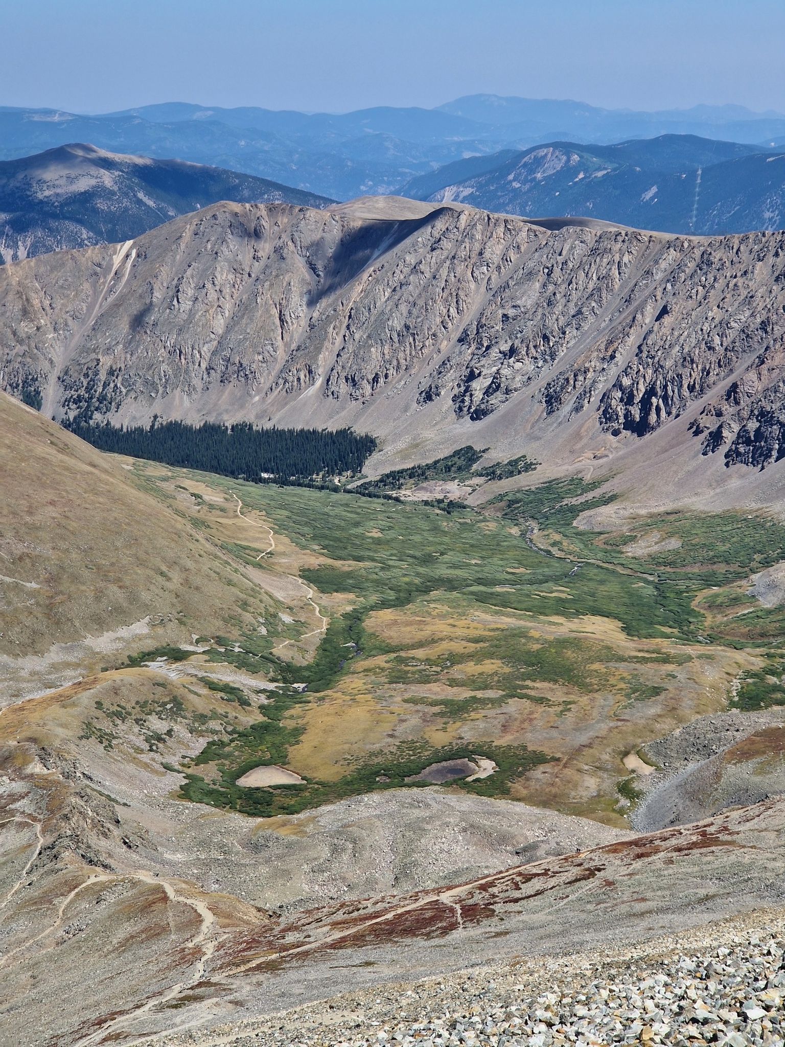 A winding path descends into a green mountain valley with a small lake. - Grays and Torreys Peak Trail