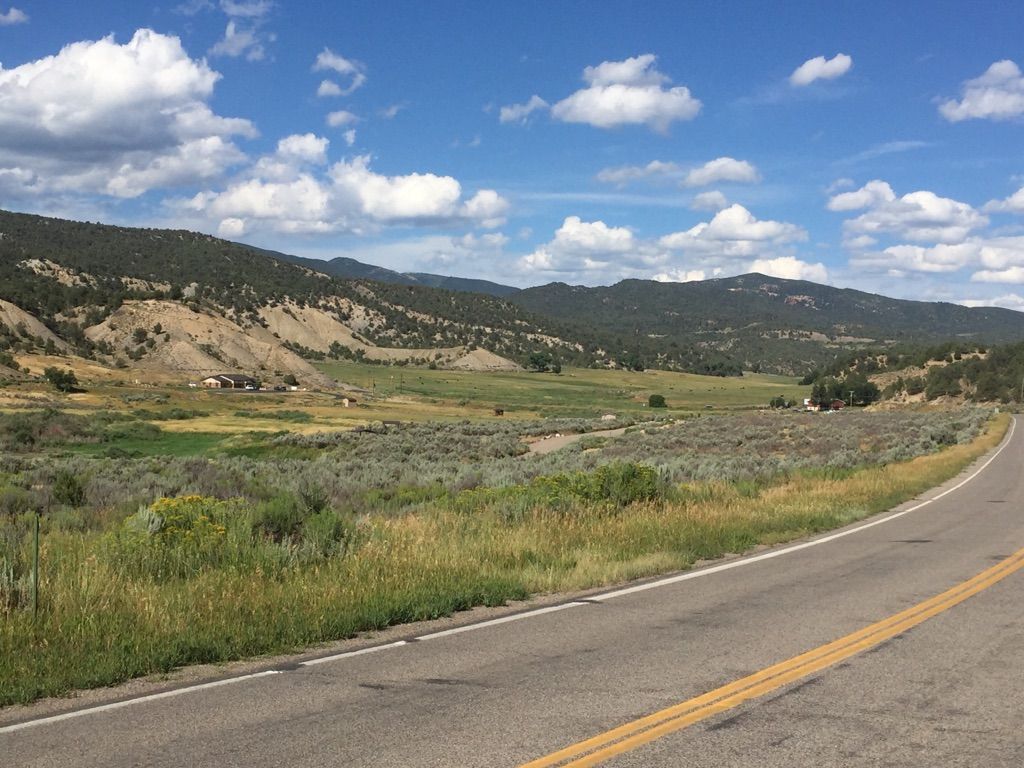 A paved road curves through a wide valley with distant mountains. - Rifle Gap Reservoir – New Castle loop from New Castle