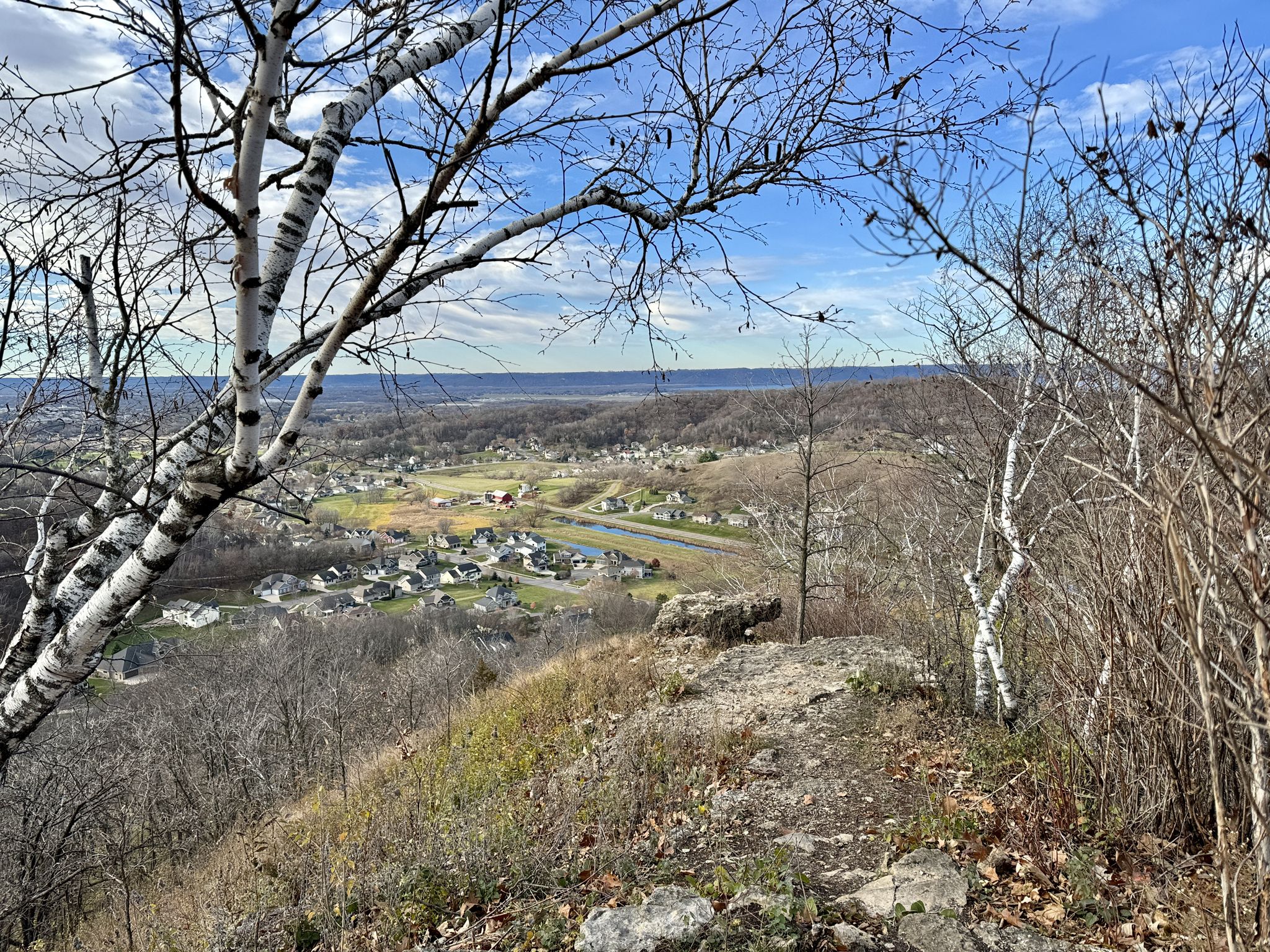 Rocky overlook with bare trees, viewing a valley town under blue sky. - Loggers Loop Trail