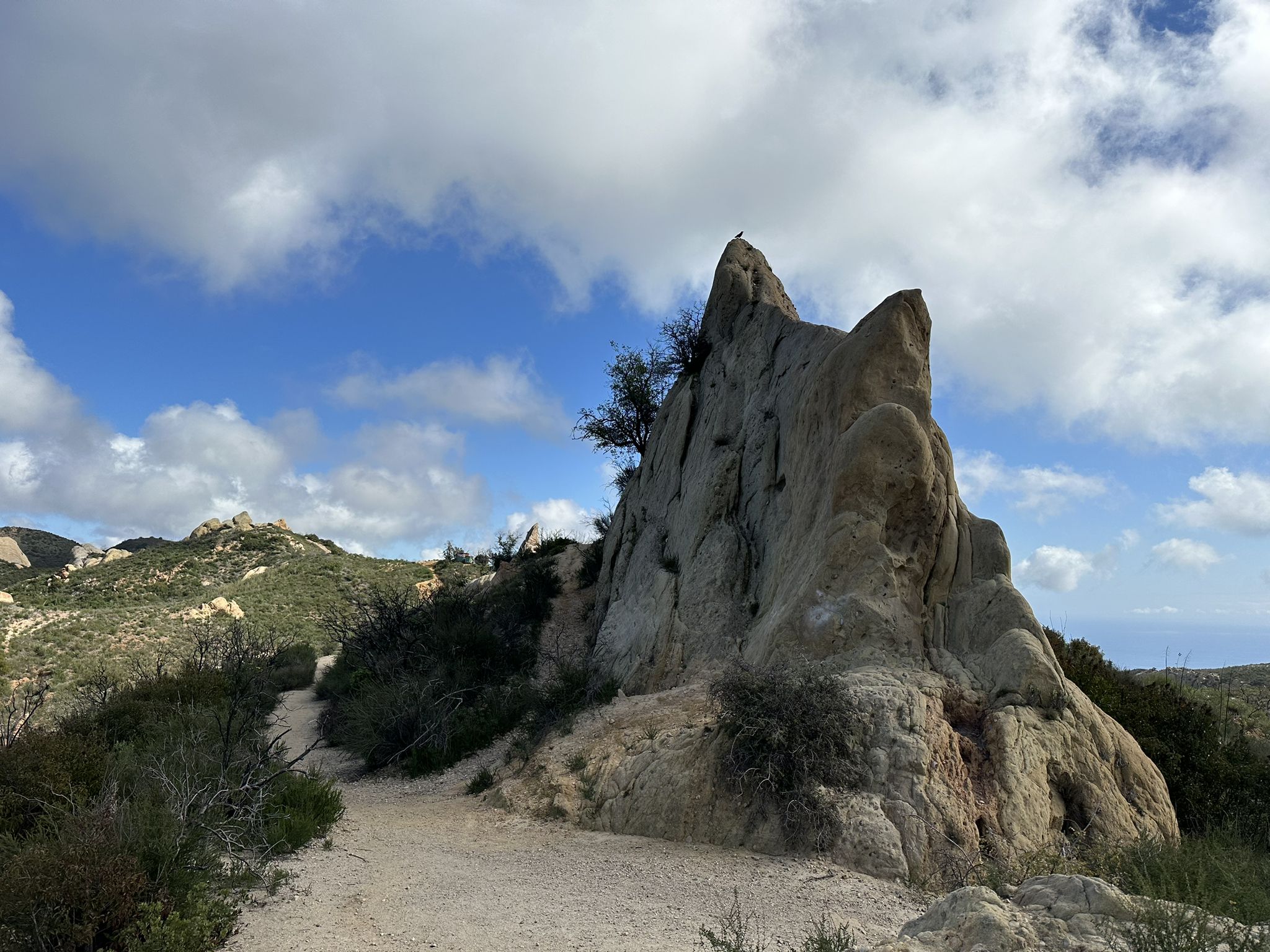 A large, jagged rock formation stands beside a dirt path under a cloudy sky. - Backbone Trail: Tapia to Kanan-Dume