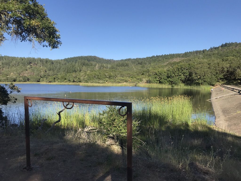 Calm lake with tall reeds, framed by hills and a metal structure. - Lake Ilsanjo via Canyon and Spring Creek Trail
