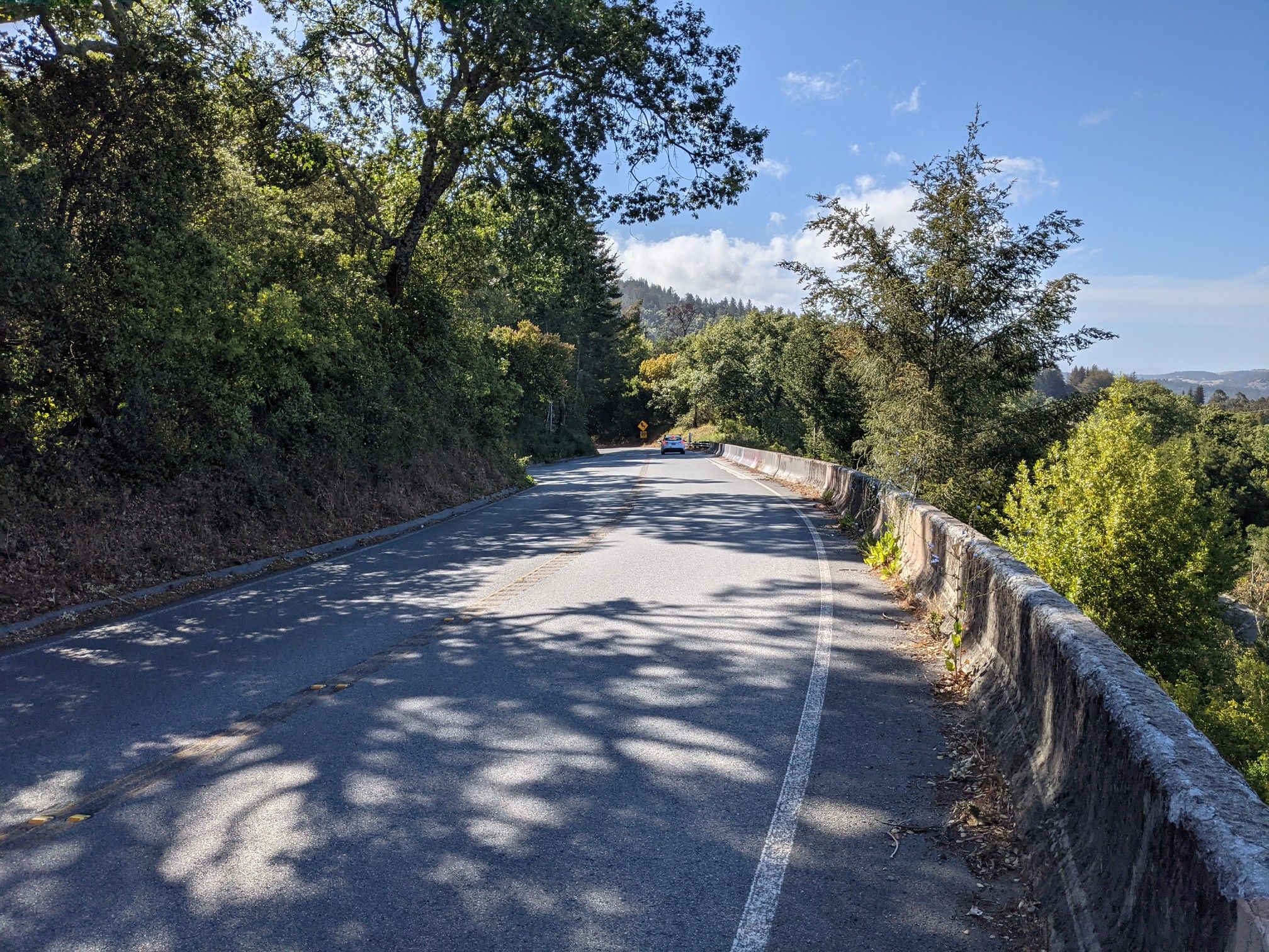 Sunny road with a concrete barrier, overlooking a forested valley. - Lower Kings Mountain Road – Kings Mountain Road loop from Palo Alto